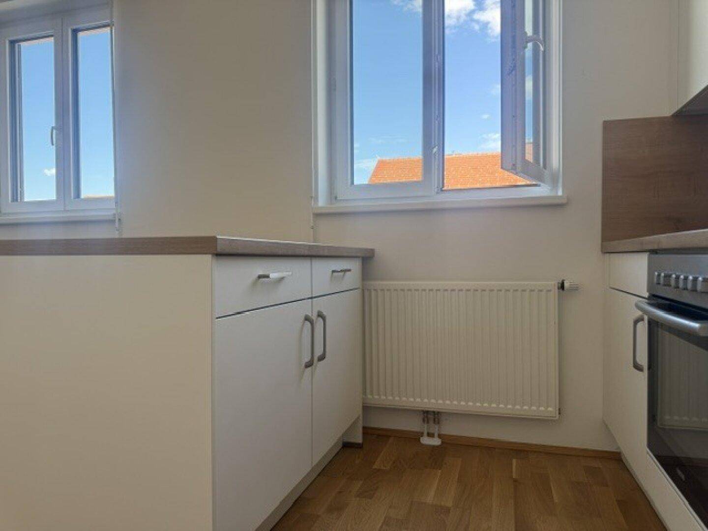 Küchenbereich mit weißer Küchenzeile, Heizkörper und zwei Fenstern für viel Tageslicht.