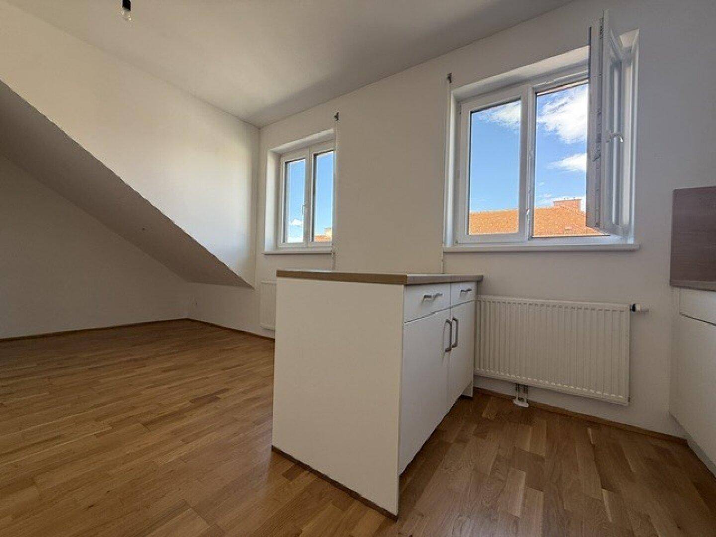 Heller Wohnbereich mit Holzboden, Dachschräge und zwei Fenstern, die viel Licht spenden.