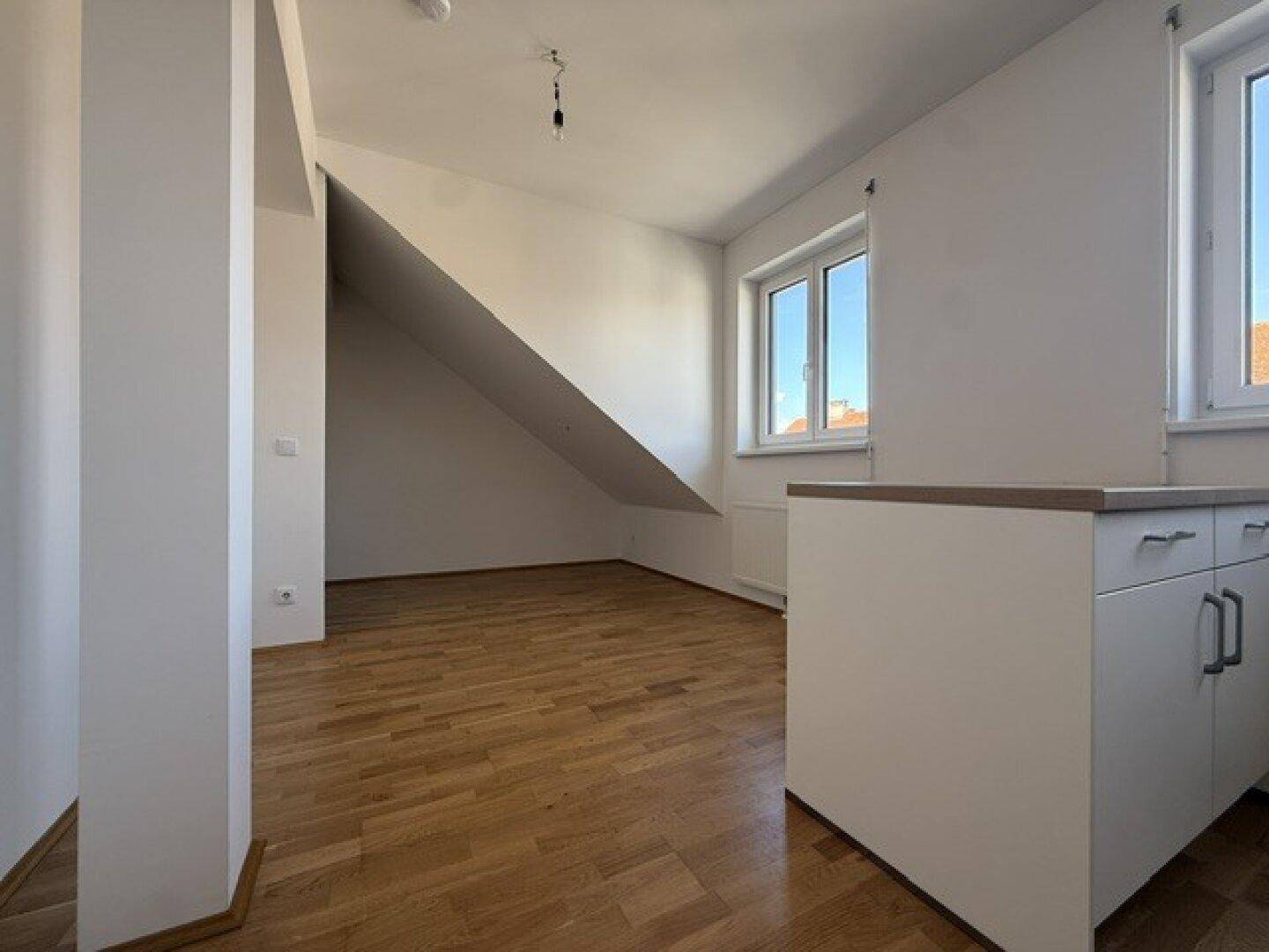 Geräumiger Wohnbereich mit Holzboden, Dachschräge und einem Fenster, das den Raum erhellt.