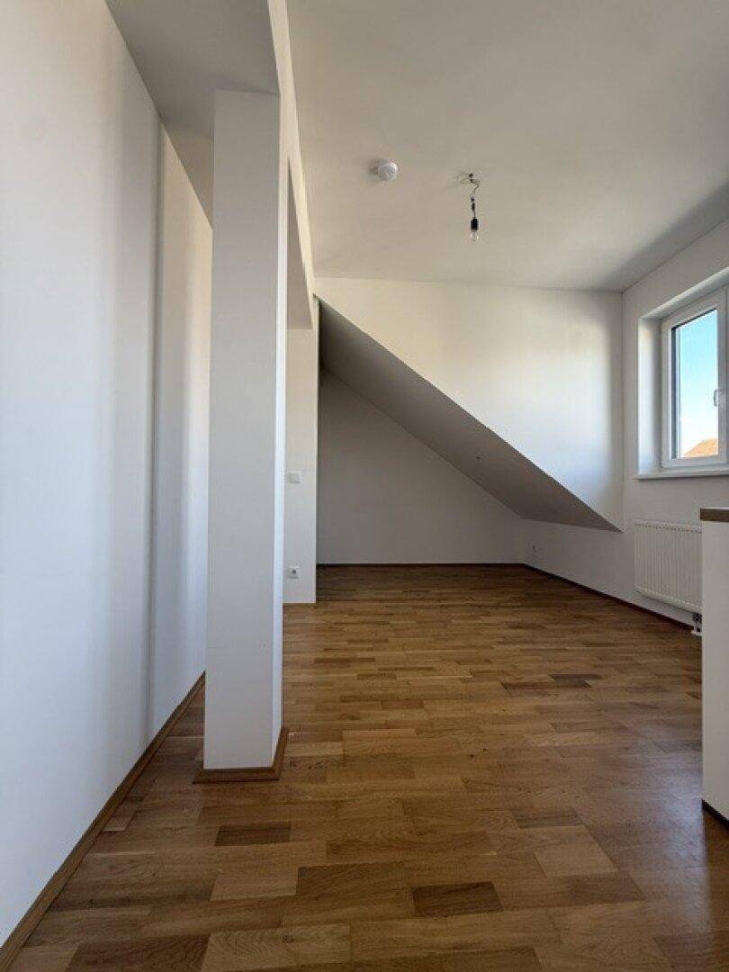Heller Wohnraum mit Holzboden, weiß gestrichenen Wänden und einer markanten Dachschräge.