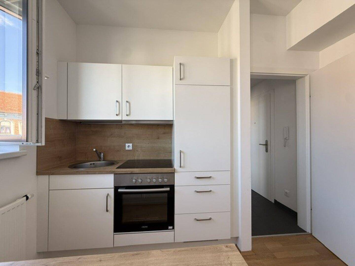Kompakte Einbauküche mit weißen Schränken, Kochfeld und Backofen, angrenzend an den Flur.