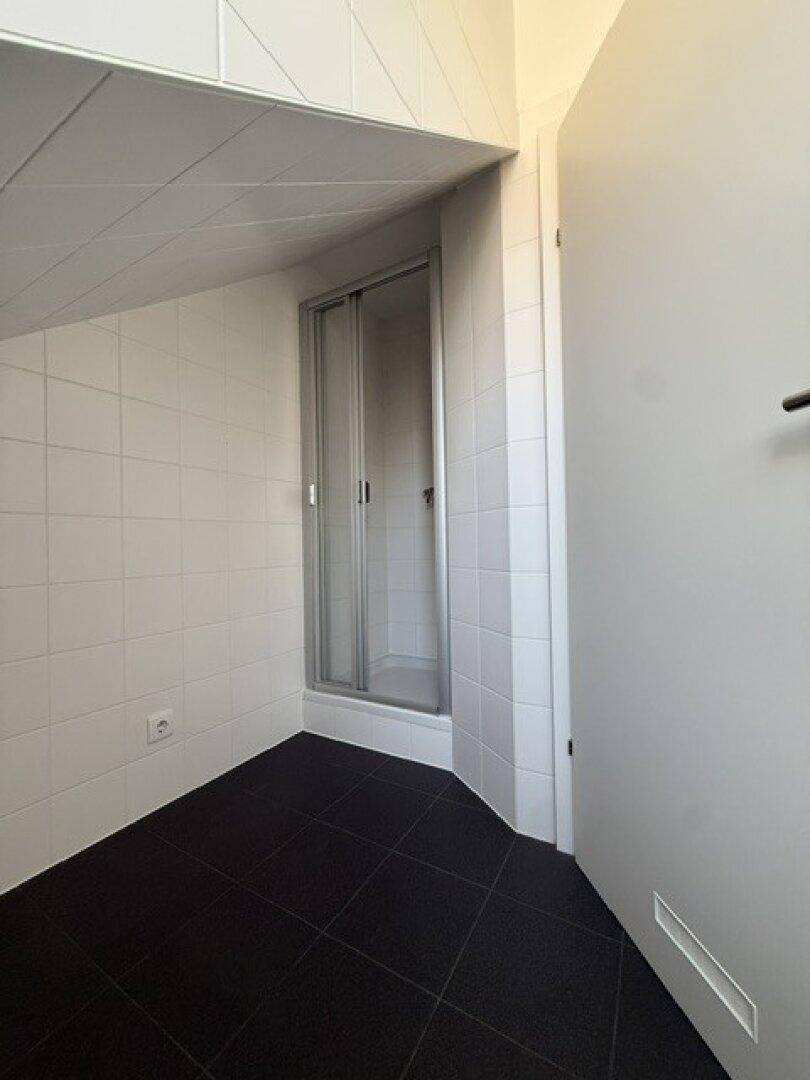Badezimmer mit weißen Wandfliesen, dunklem Boden und einer Duschkabine in der Ecke.