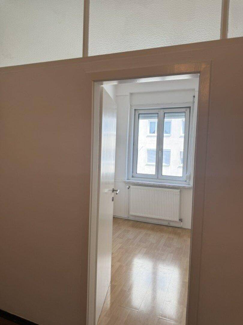 Blick durch eine Tür in einen hellen Raum mit Fenster und Heizkörper.
