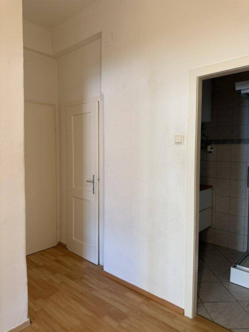 Flur mit hellem Holzfußboden und Zugang zu einem Badezimmer mit Fliesen.