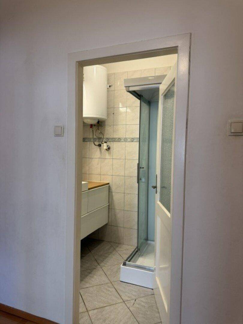 Badezimmer mit Fliesenboden, modernem Waschtisch, Duschkabine und Warmwasserboiler.