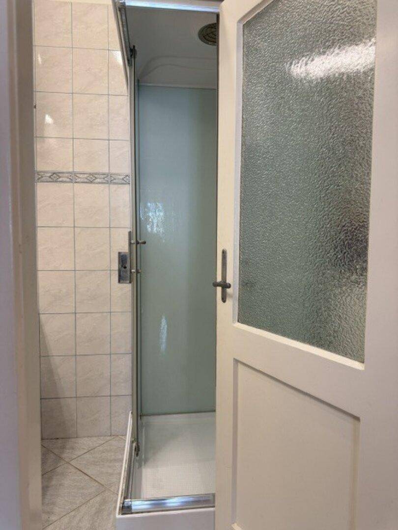 Duschkabine mit gefliesten Wänden und Milchglastür im Badezimmer.