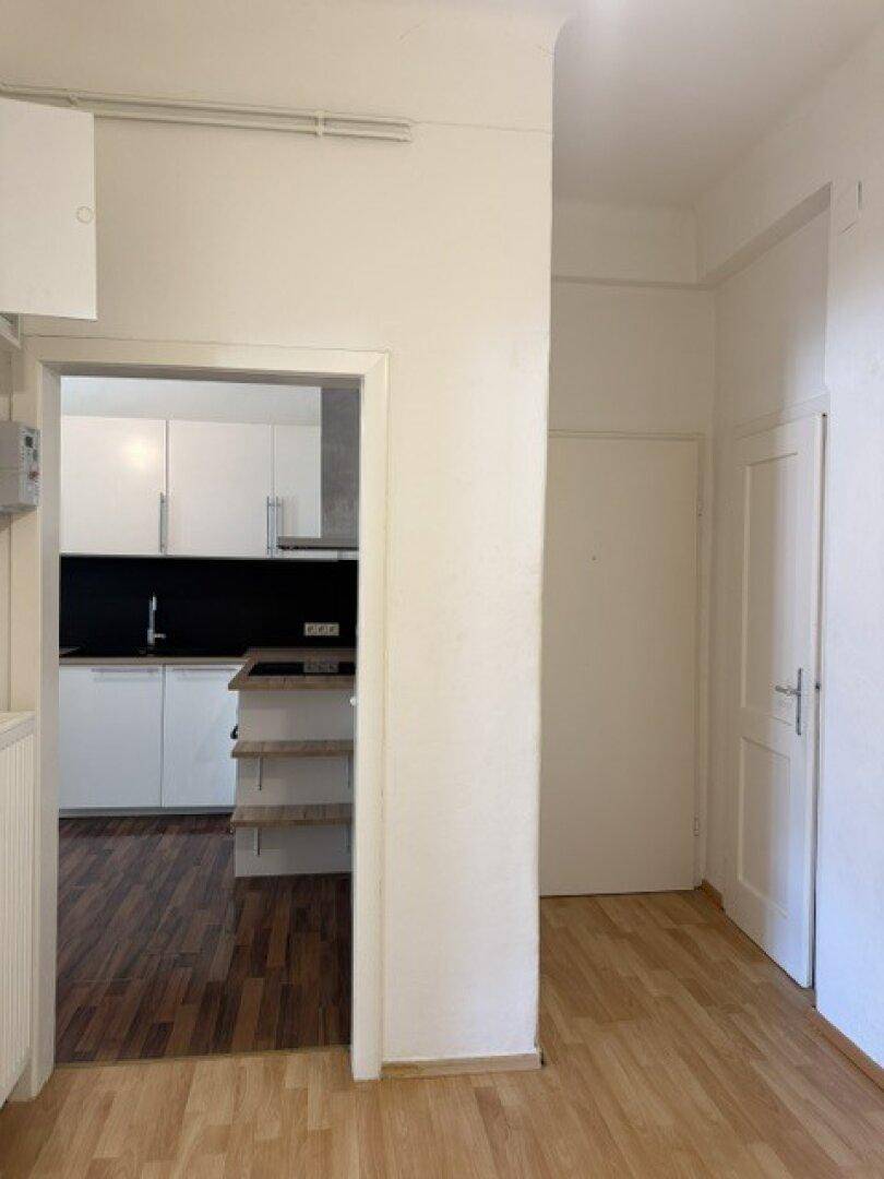 Heller Flur mit Holzfußboden und Blick in eine moderne Küche mit weißen Schränken.