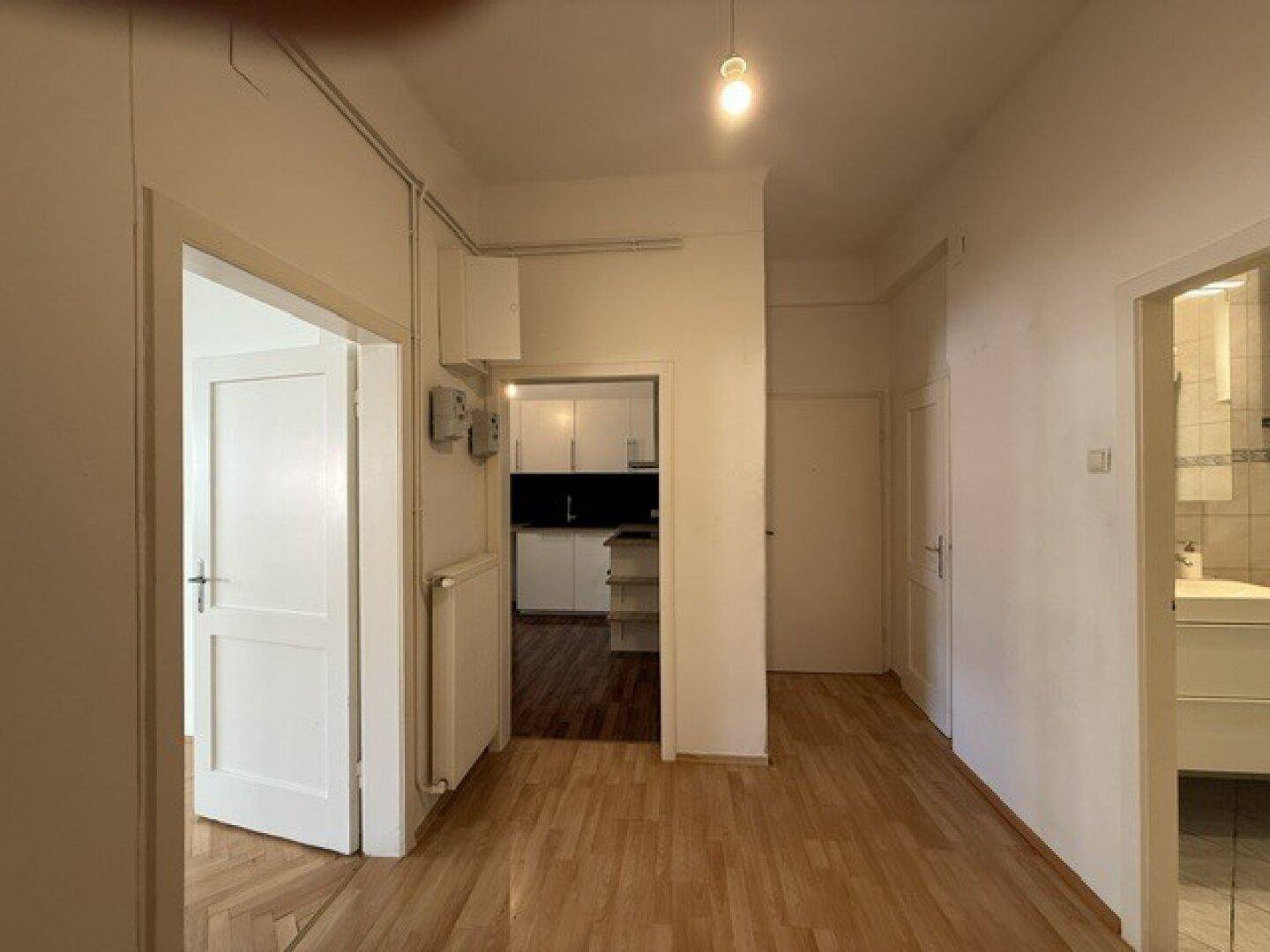 Heller Flur mit Holzfußboden und Zugang zu Küche und Badezimmer.