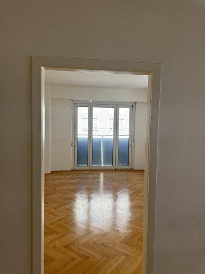 Blick in einen hellen Raum mit Fischgrätparkett und großen Glastüren zum Außenbereich.