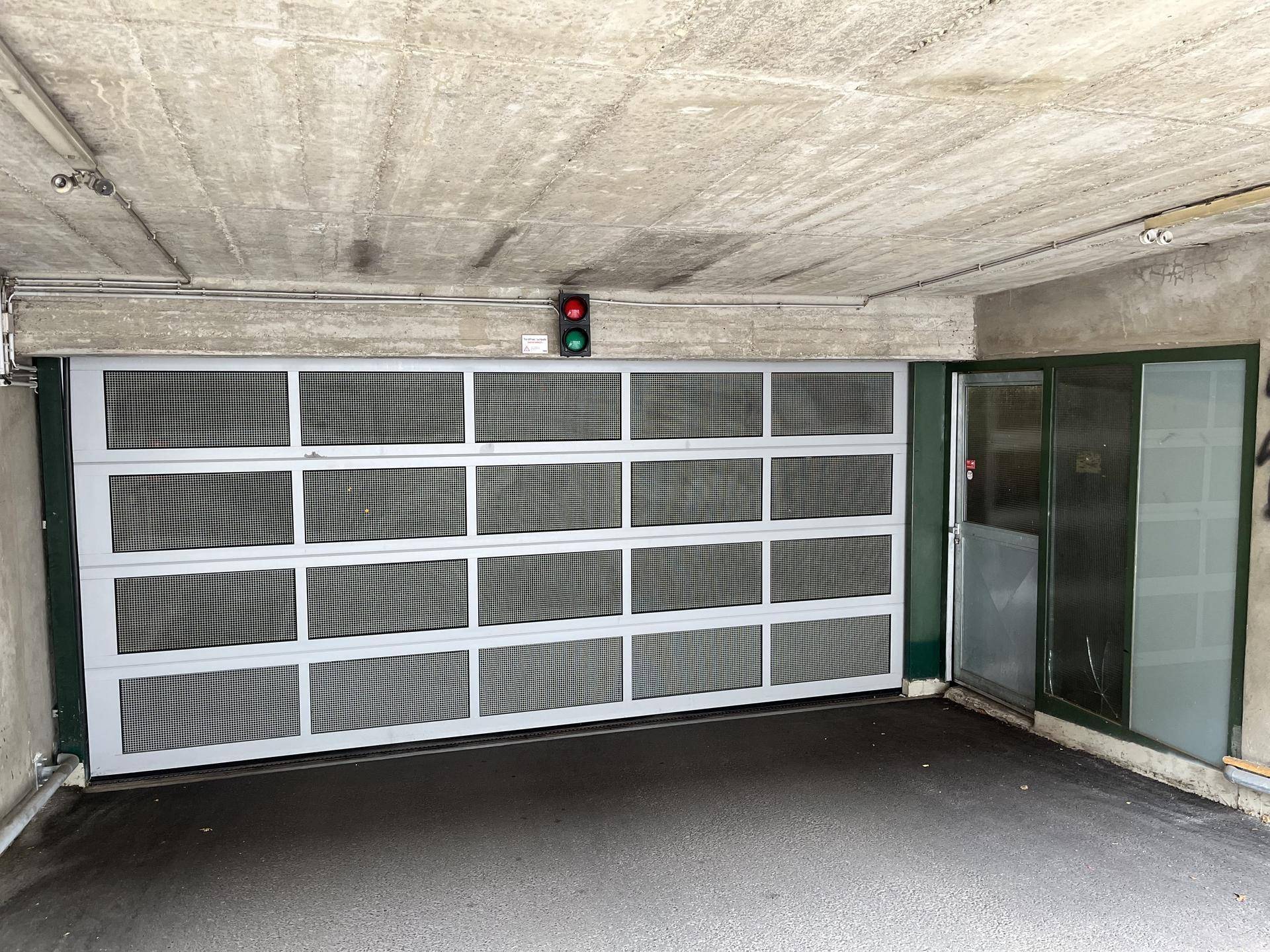 Eingang zur Tiefgarage mit modernem Sektionaltor, integrierter Fußgängertür und Ampelregelung.
