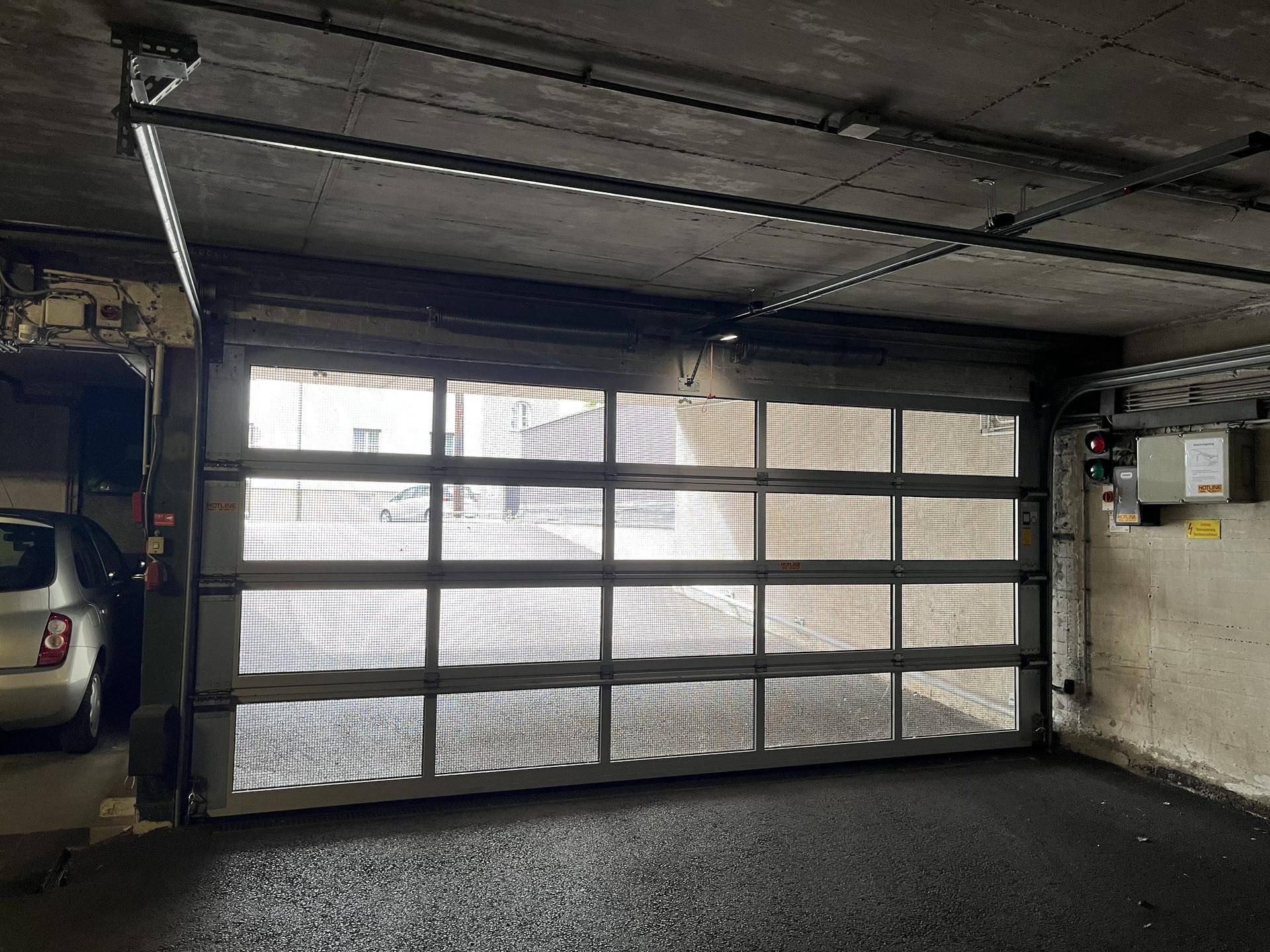 Blick aus der Tiefgarage durch das Sektionaltor mit Glaspaneelen auf den Außenbereich und ein geparktes Auto.