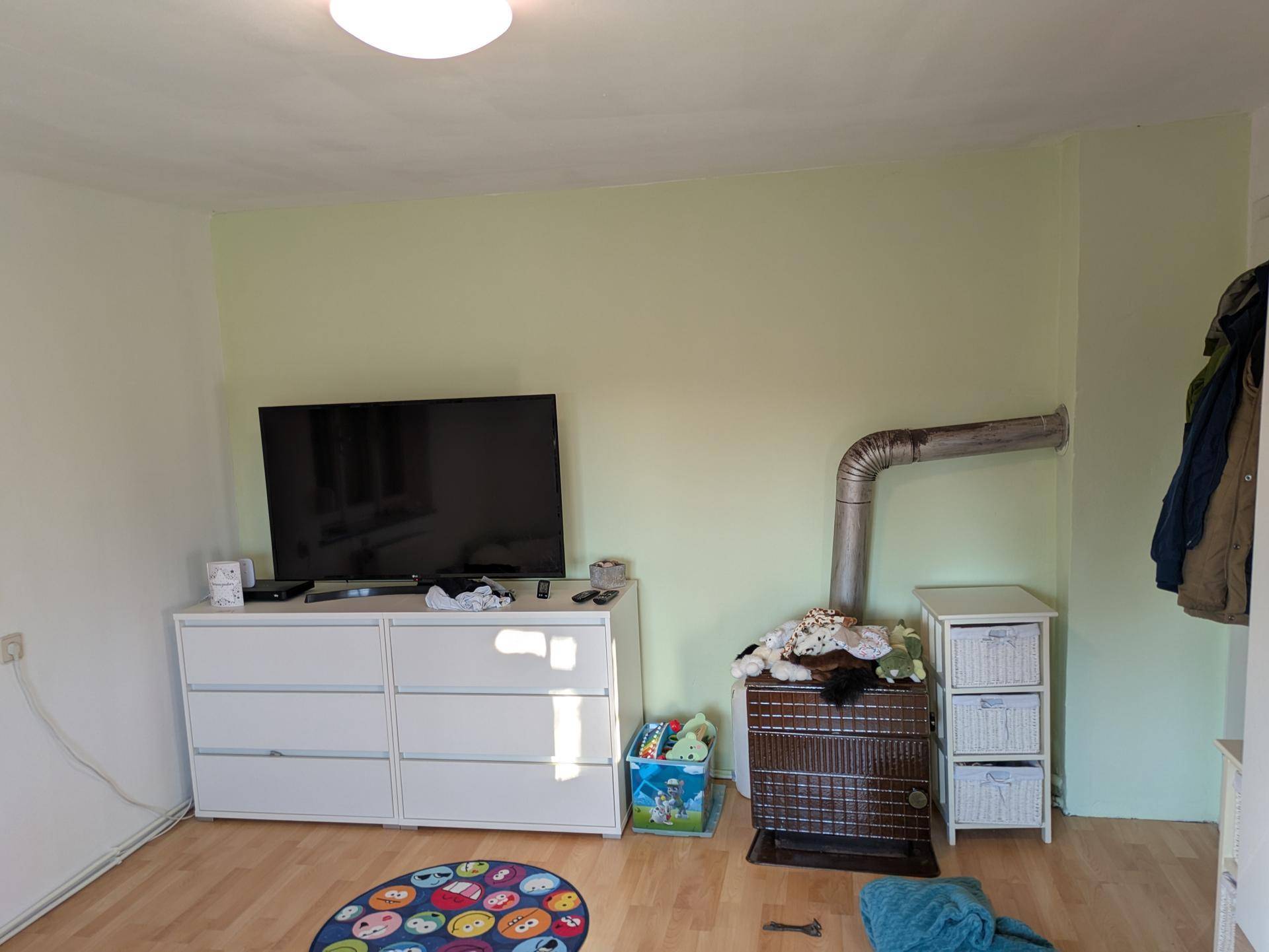 Gemütlicher Wohnraum mit hellem Holzboden, Fernseher und einem Holzofen als Heizquelle.