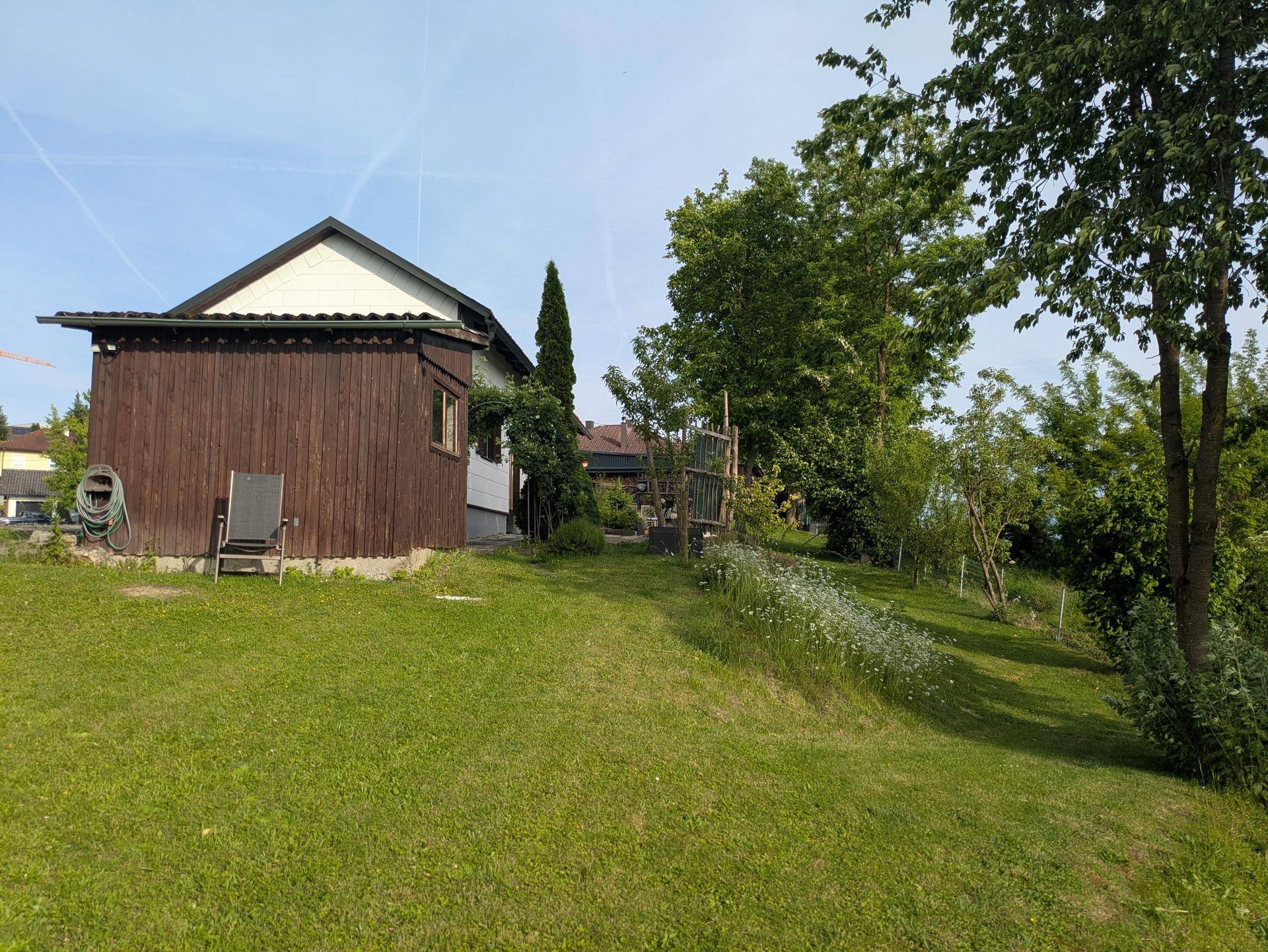 Seitenansicht eines Holzhauses mit Rasenfläche und Bäumen in einer ruhigen Umgebung.