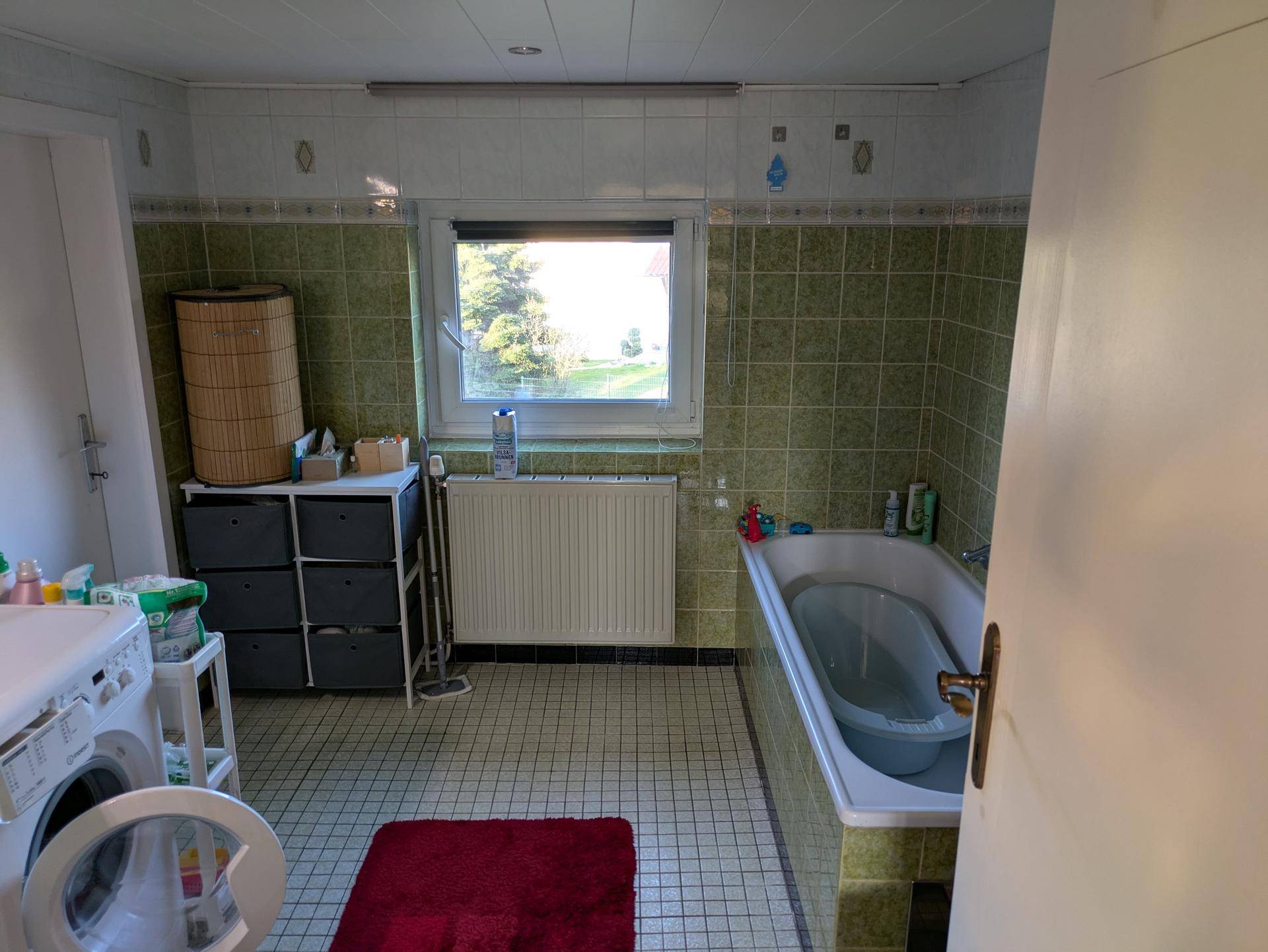 Badezimmer mit grünen Fliesen, Badewanne und Fenster, in gutem, aber älterem Zustand.