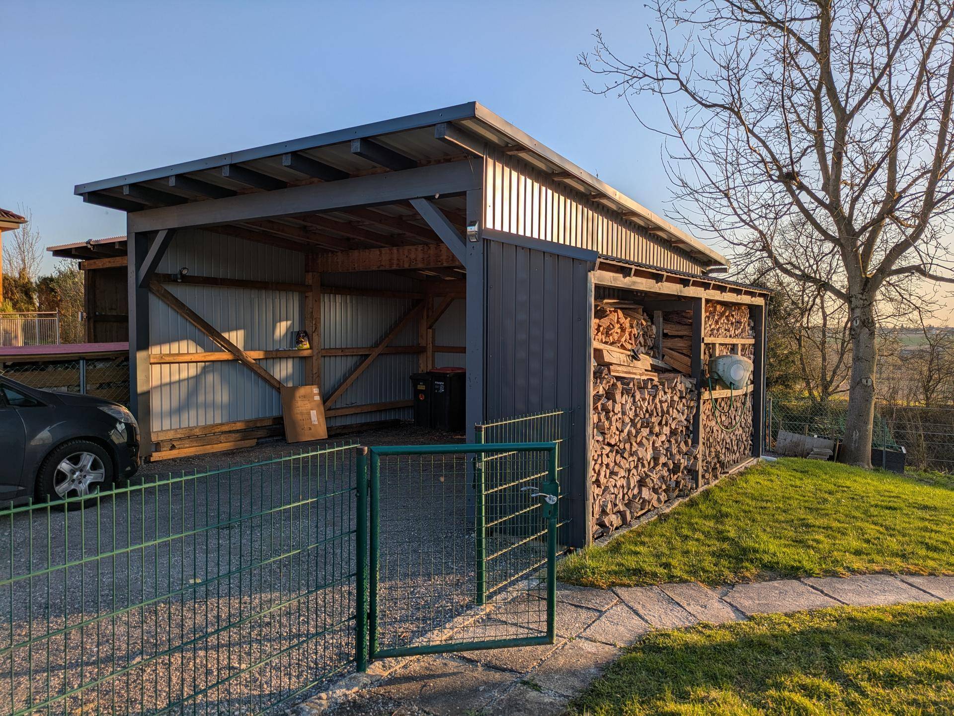 Geräumiger Carport mit integriertem Holzschuppen und Lagerplatz für Brennholz.