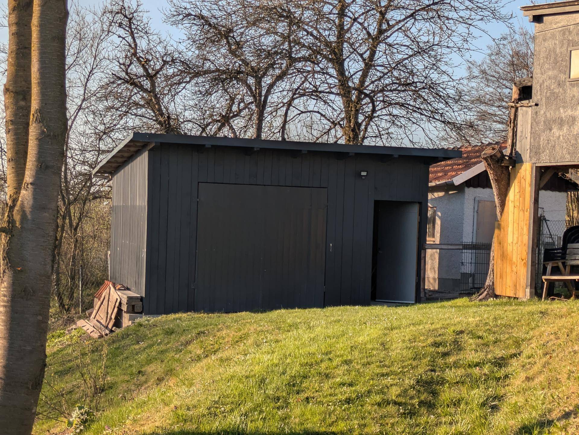 Dunkelgraue Garage oder Schuppen mit Flachdach auf einer grünen Rasenfläche.