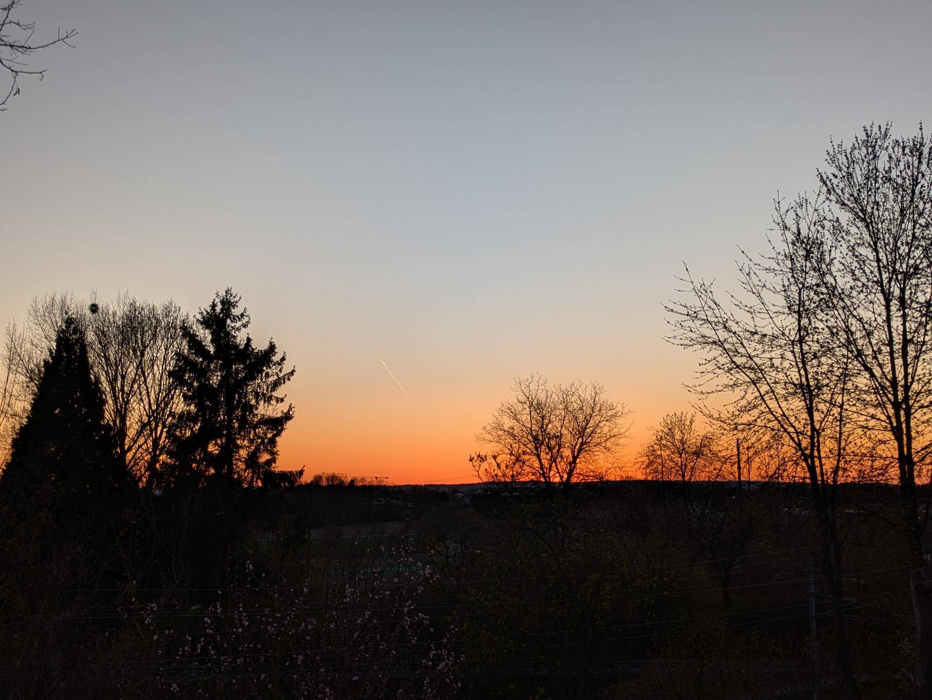 Malerischer Sonnenuntergang über der ländlichen Landschaft mit Silhouette von Bäumen am Horizont.
