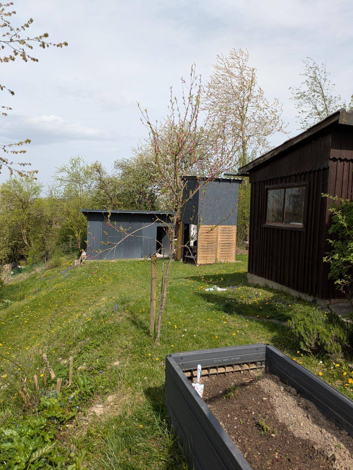 Gartenbereich mit Hochbeet und verschiedenen Nebengebäuden in ländlicher Umgebung.