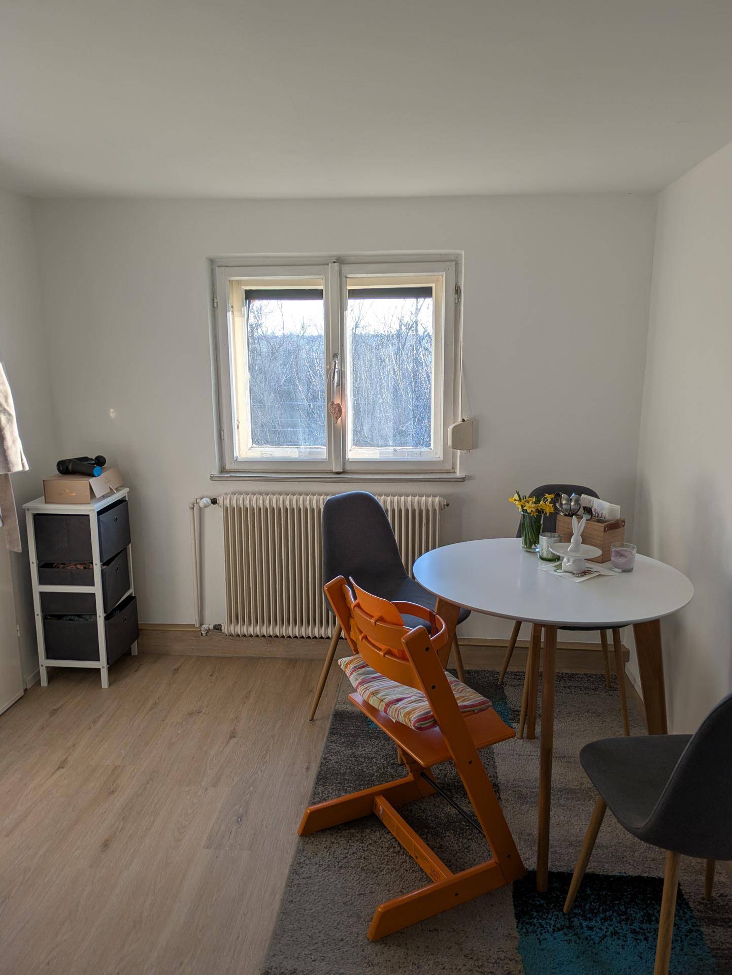 Essbereich mit hellem Holzboden, kleinem Esstisch und Stühlen neben einem Fenster.
