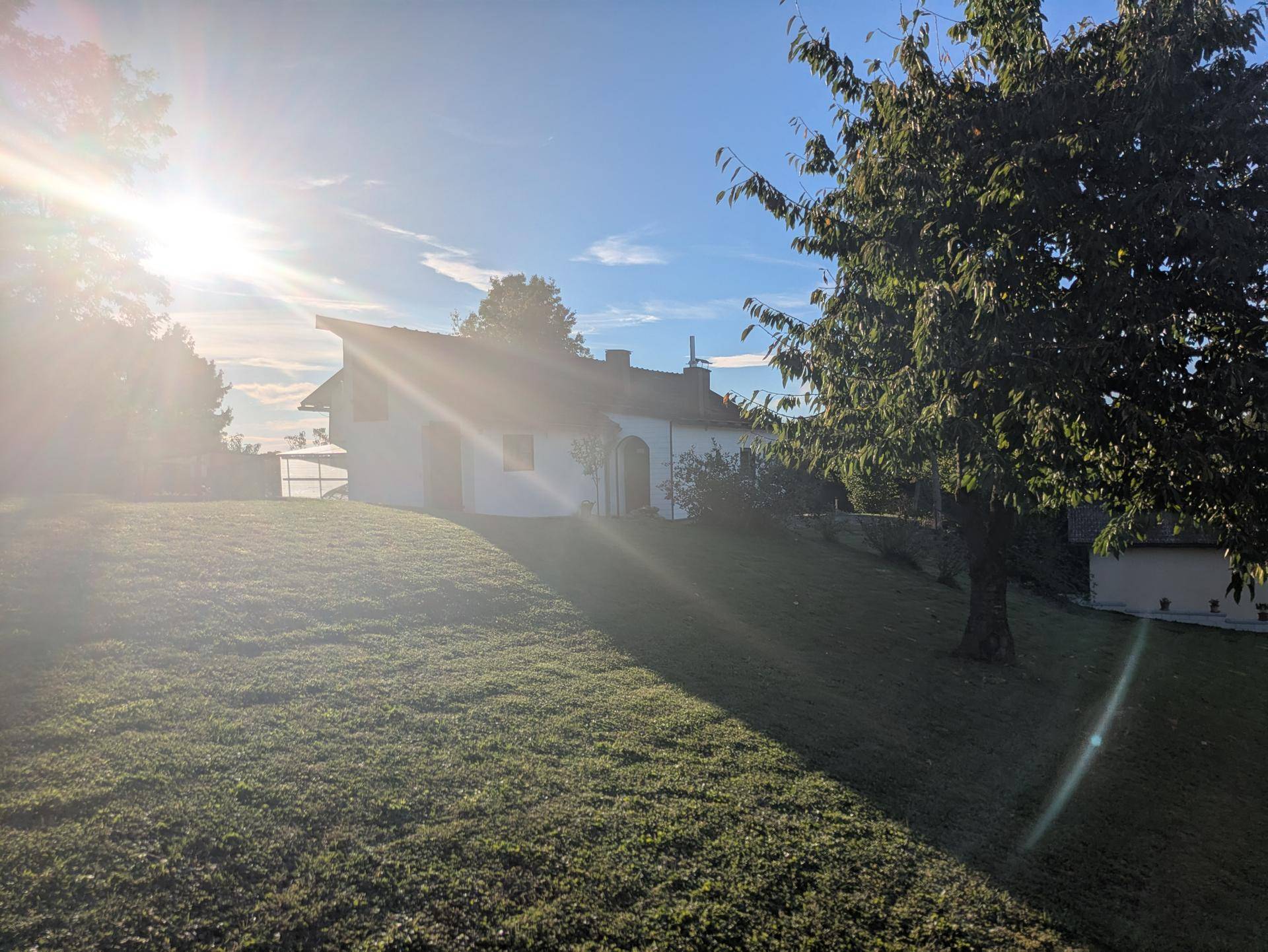 Haus in ländlicher Umgebung, umgeben von viel Grün und Bäumen unter strahlendem Sonnenschein.