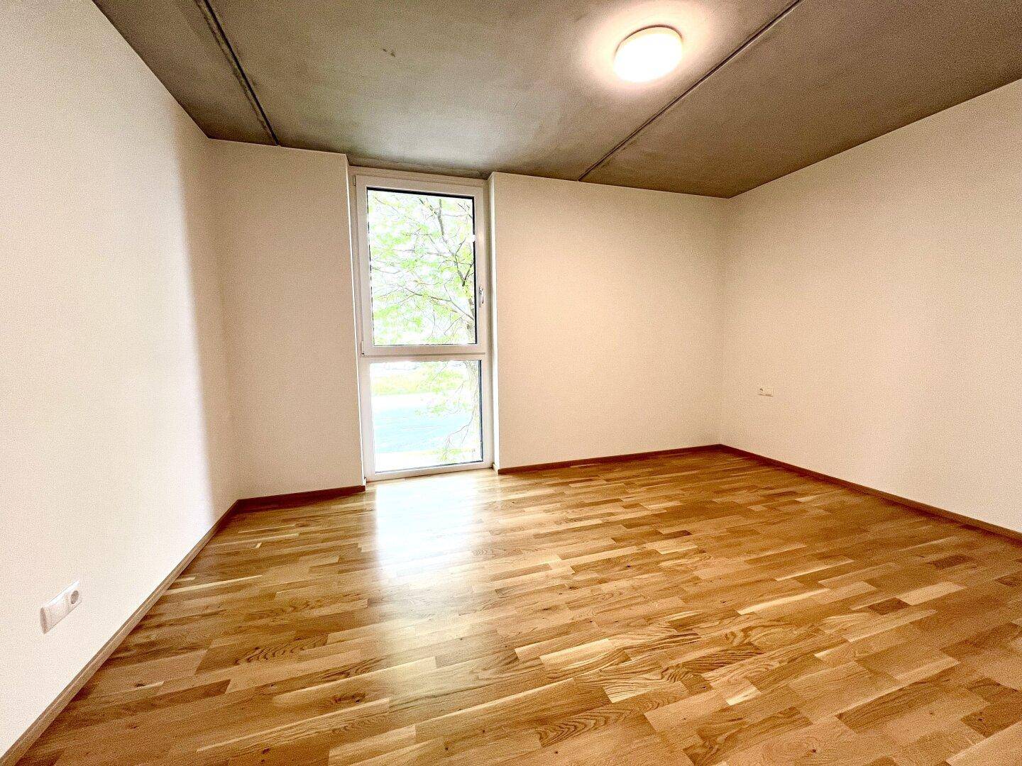 Ruhiges Schlafzimmer mit Holzboden und einem hohen Fenster, das eine grüne Aussicht bietet.