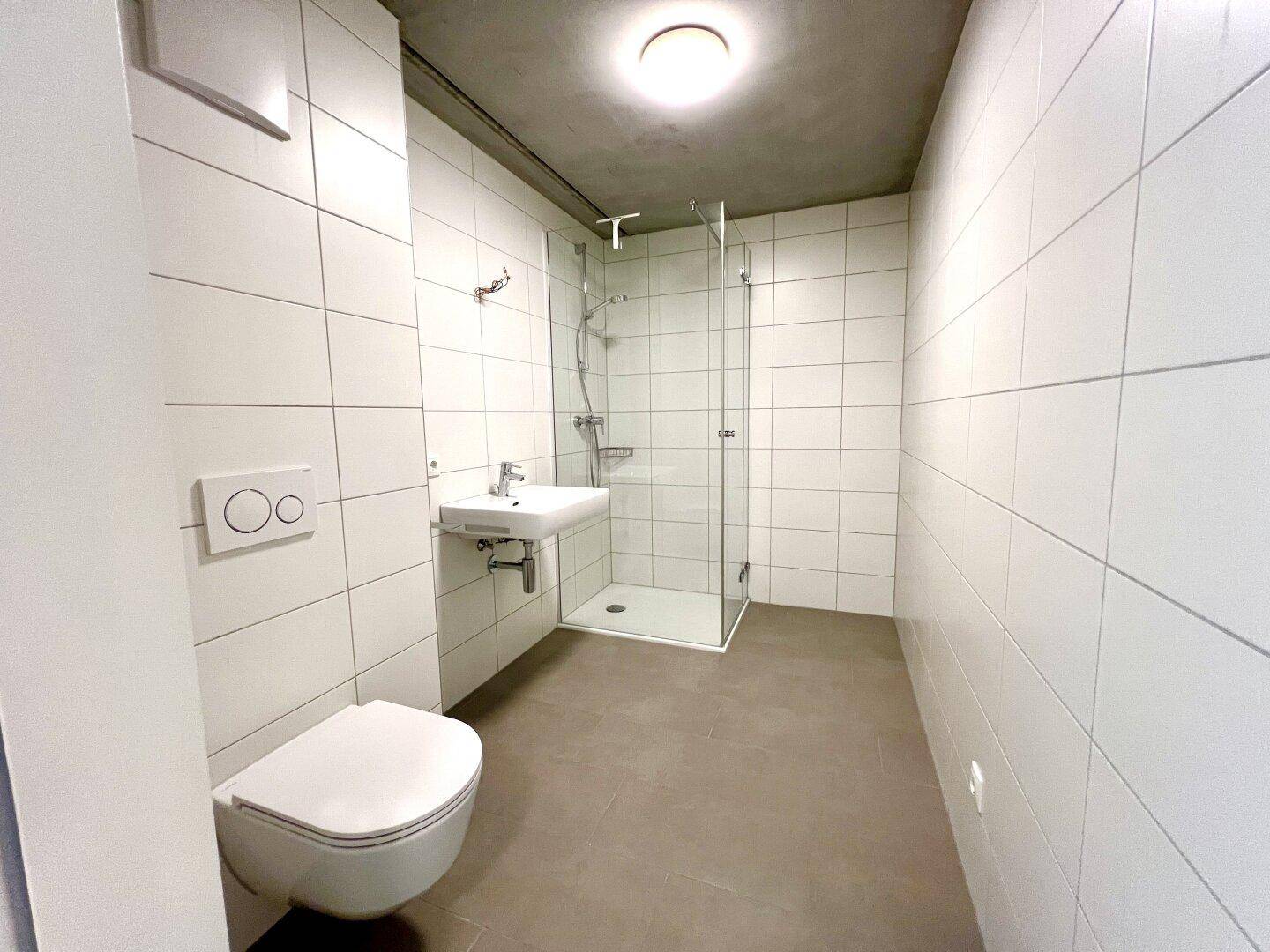 Modernes Badezimmer mit weißen Fliesen, ebenerdiger Dusche und wandhängendem WC.