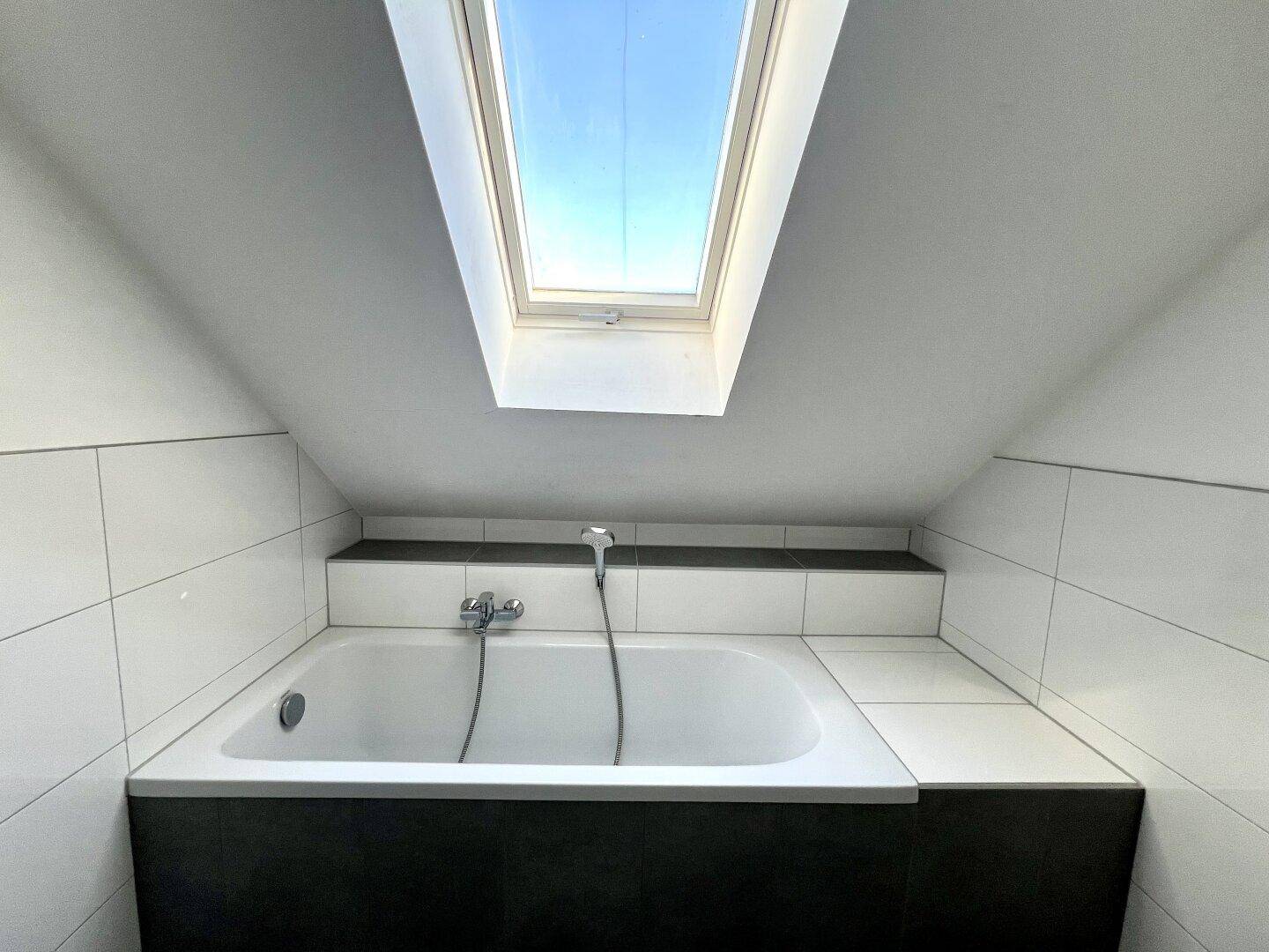 Eingebaute Badewanne mit Fliesenverkleidung und darüberliegendem Dachfenster für natürliches Licht.
