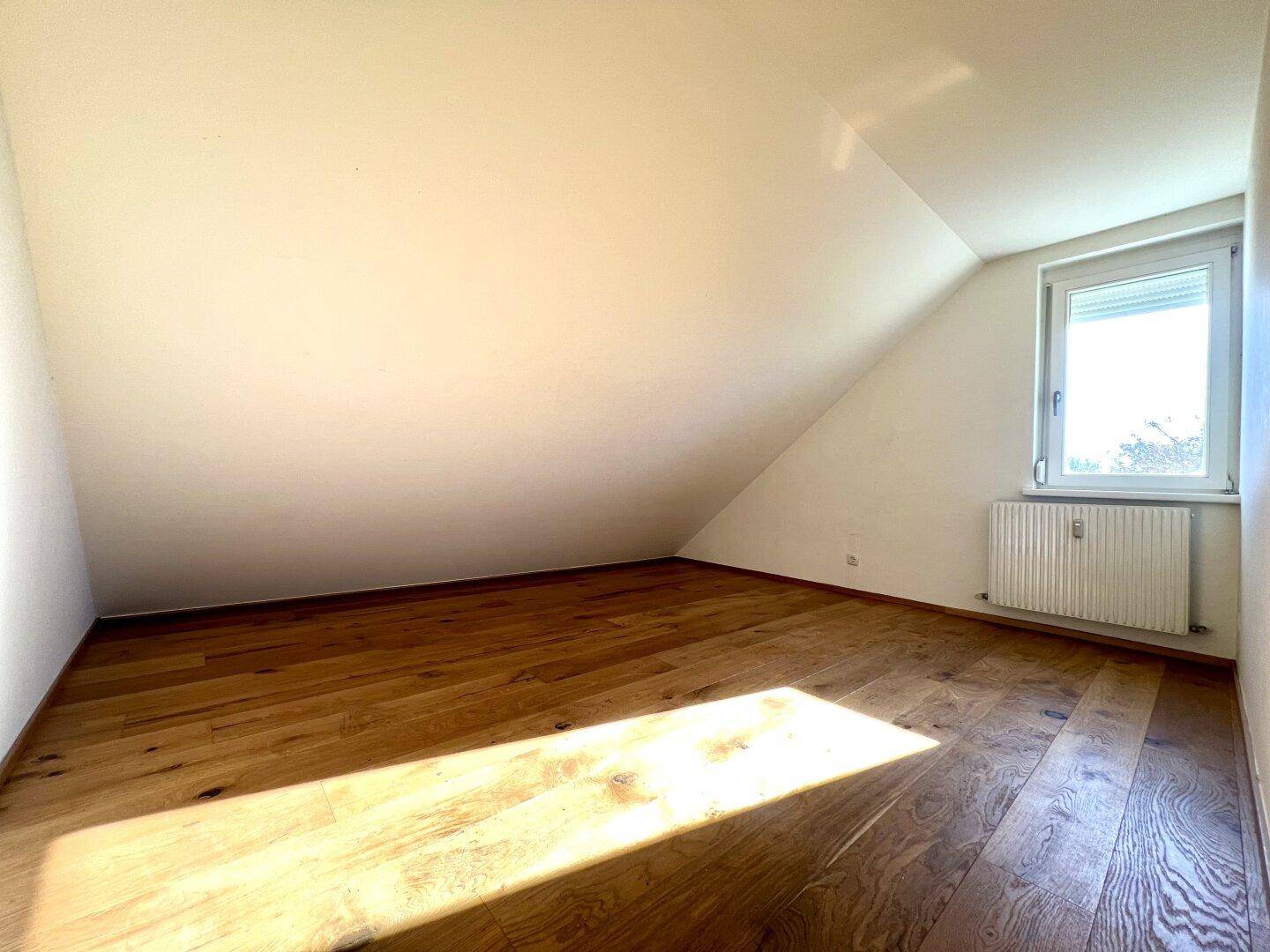 Gemütliches Schlafzimmer im Dachgeschoss mit Holzboden, schräger Decke und Fenster.
