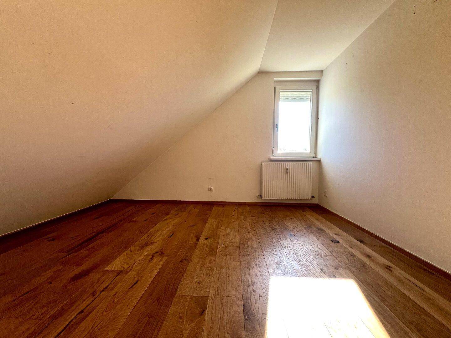 Ruhiges Schlafzimmer im Dachgeschoss mit Holzboden, schräger Decke und Fenster.