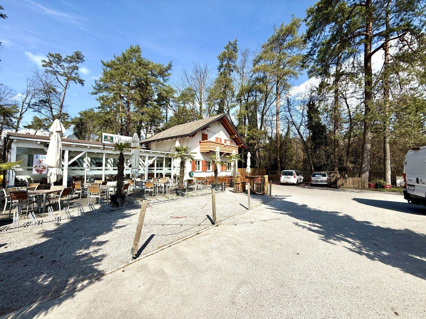 Panoramablick auf das Gasthaus mit sonniger Terrasse und angrenzendem Waldgebiet.