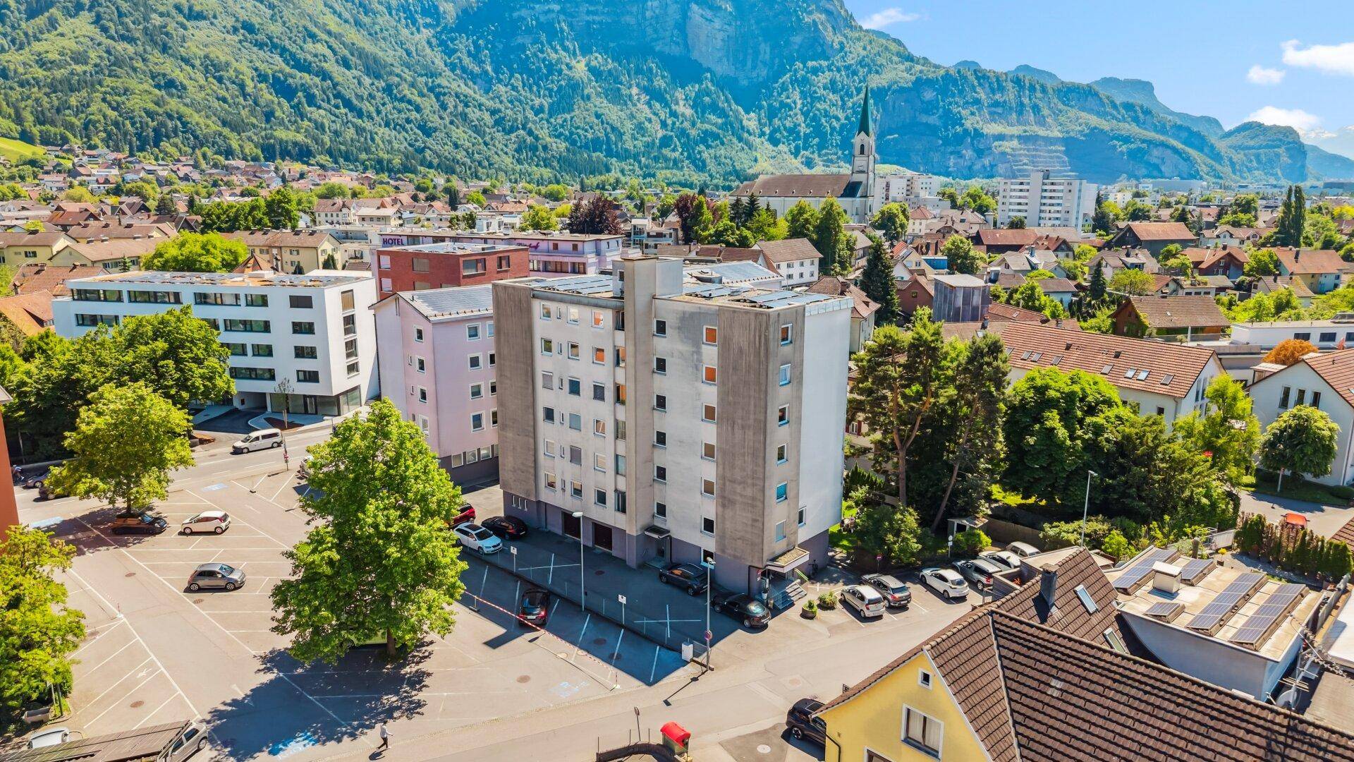 Luftaufnahme eines Wohngebäudes in einer städtischen Umgebung mit Bergen im Hintergrund.