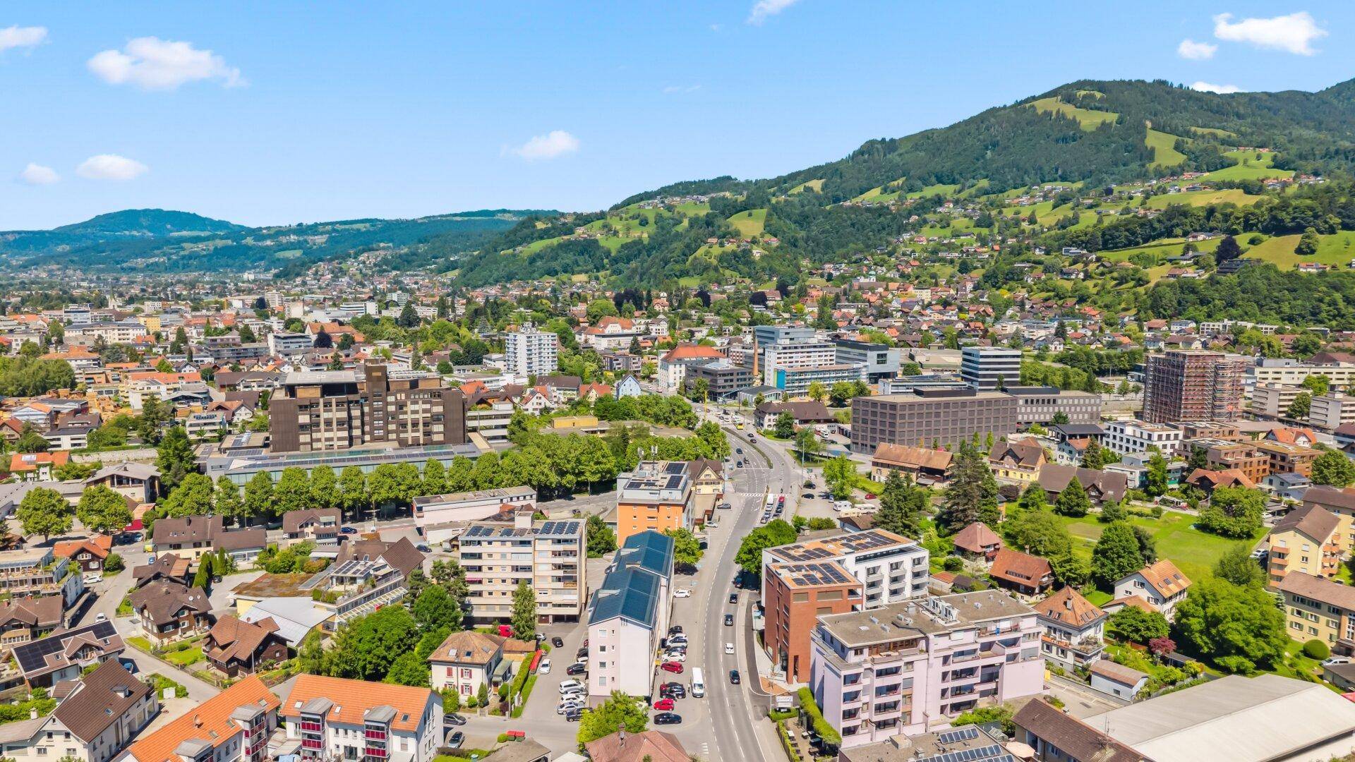 Umfassender Blick auf eine städtische Siedlung mit verschiedenen Gebäudetypen und bewaldeten Hügeln.