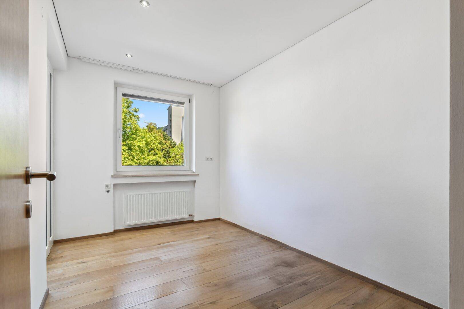 Leeres Schlafzimmer mit Holzboden, weiß gestrichenen Wänden und Fenster.