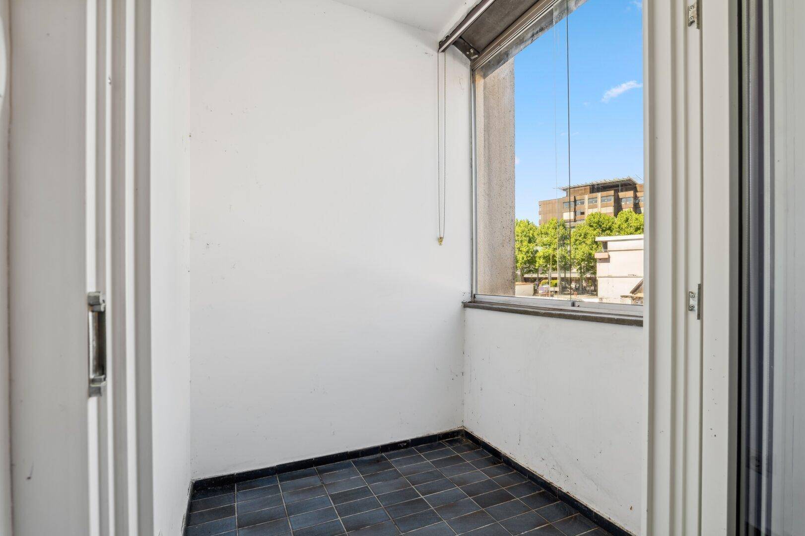 Kleiner verglaster Balkon mit Fliesenboden und Blick auf die Stadt.