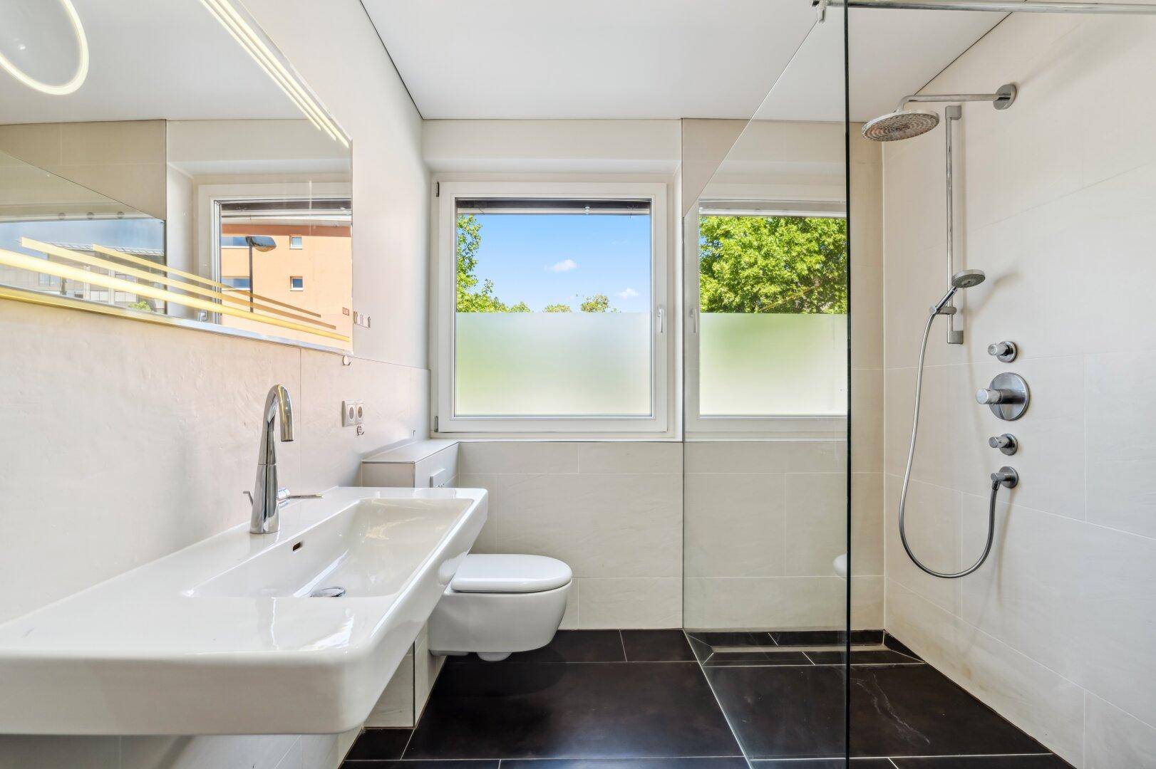 Helles Badezimmer mit großer Dusche, wandhängendem WC und Fenster.