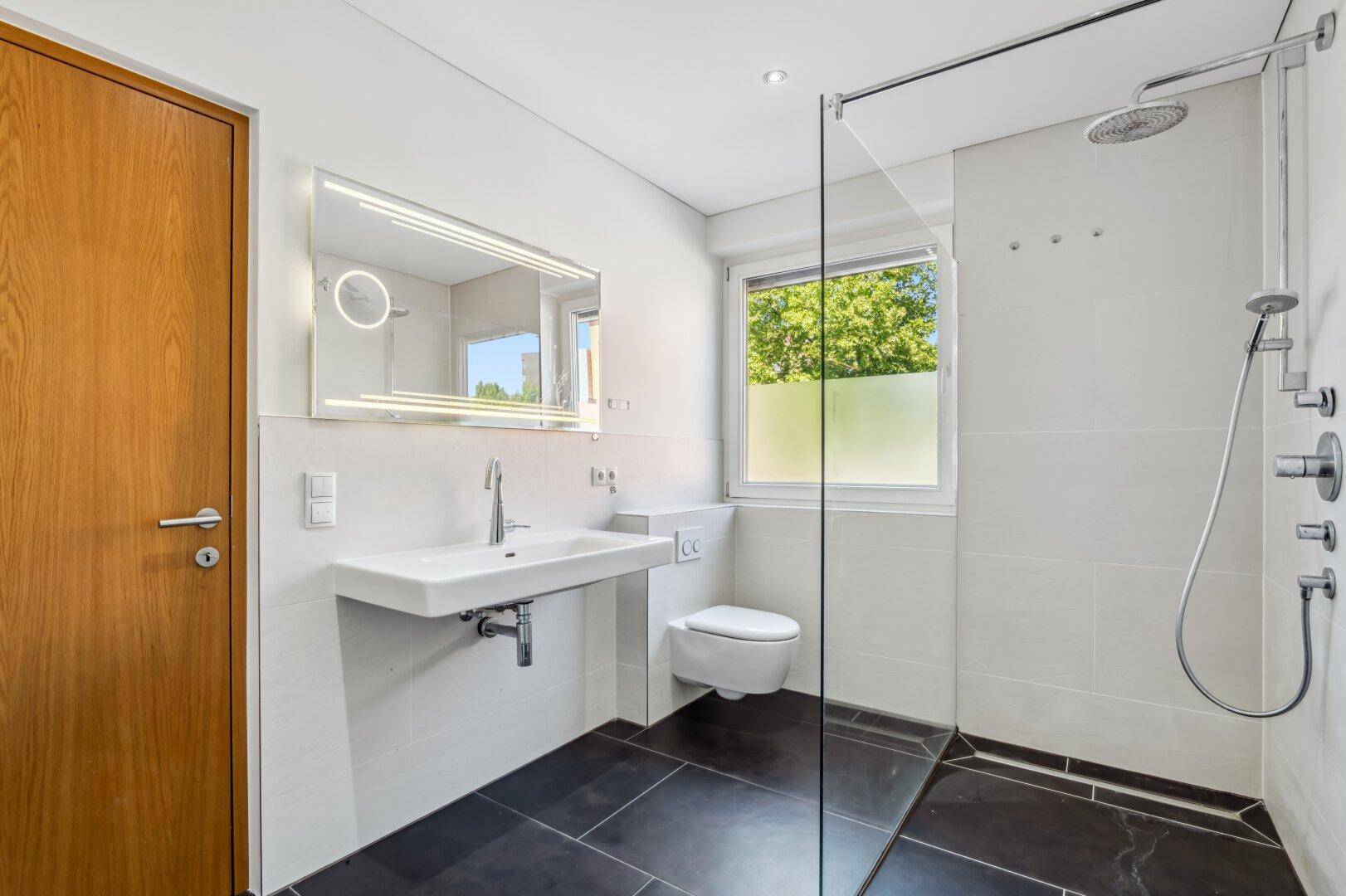 Elegantes Badezimmer mit großer Dusche, modernem Waschbecken und beleuchtetem Spiegel.