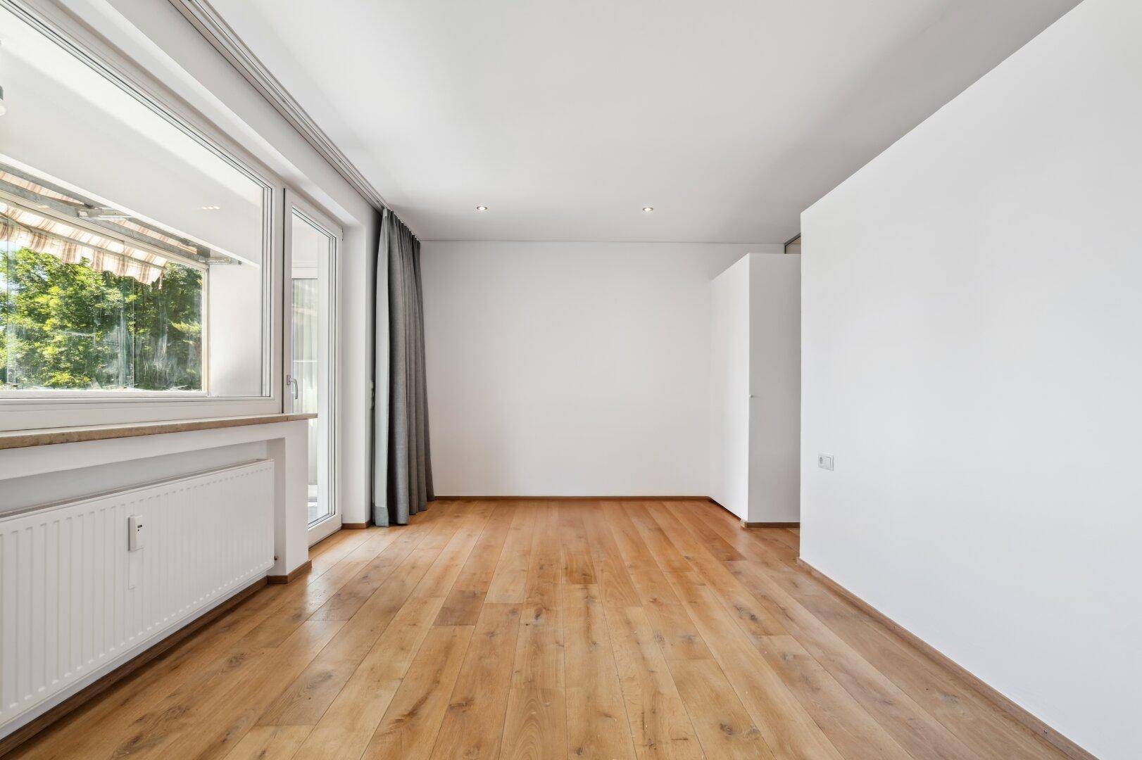 Geräumiges Schlafzimmer mit Holzboden, weißen Wänden und Zugang zum Balkon.