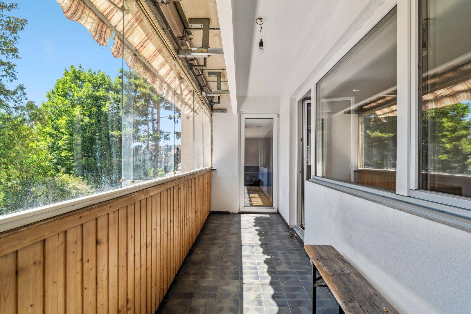 Verglaster Balkon mit Holzboden und Markise, bietet Schutz und Ausblick.