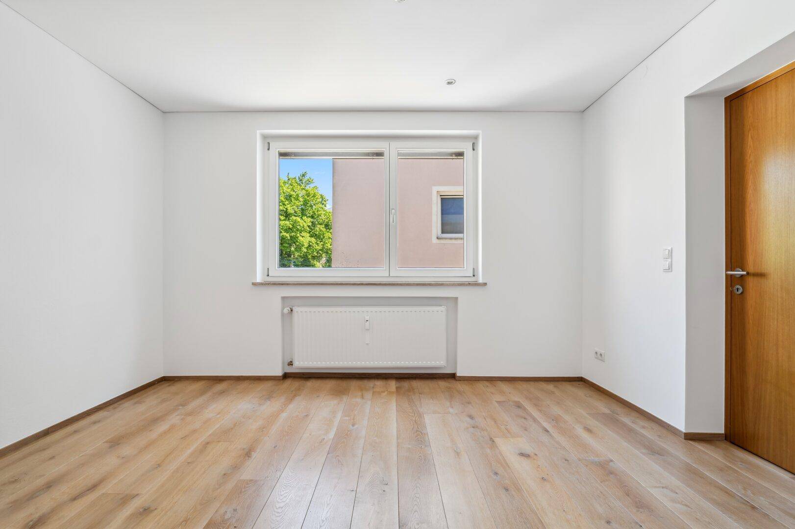 Helles Schlafzimmer mit Holzboden, weiß gestrichenen Wänden und Fenster.