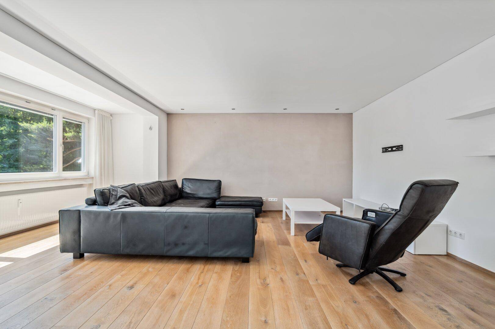 Moderner Wohnbereich mit dunklem Ledersofa und hellem Holzboden.