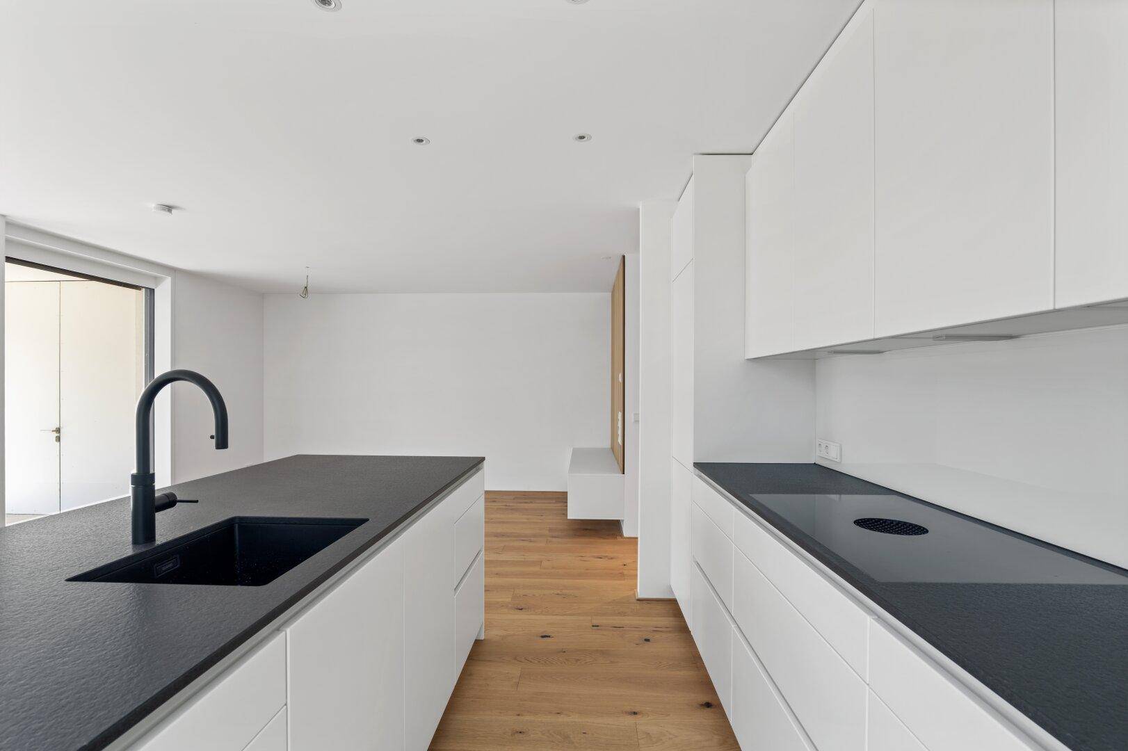 Moderne, offene Küche mit weißen Schränken, schwarzer Arbeitsplatte und Holzboden.