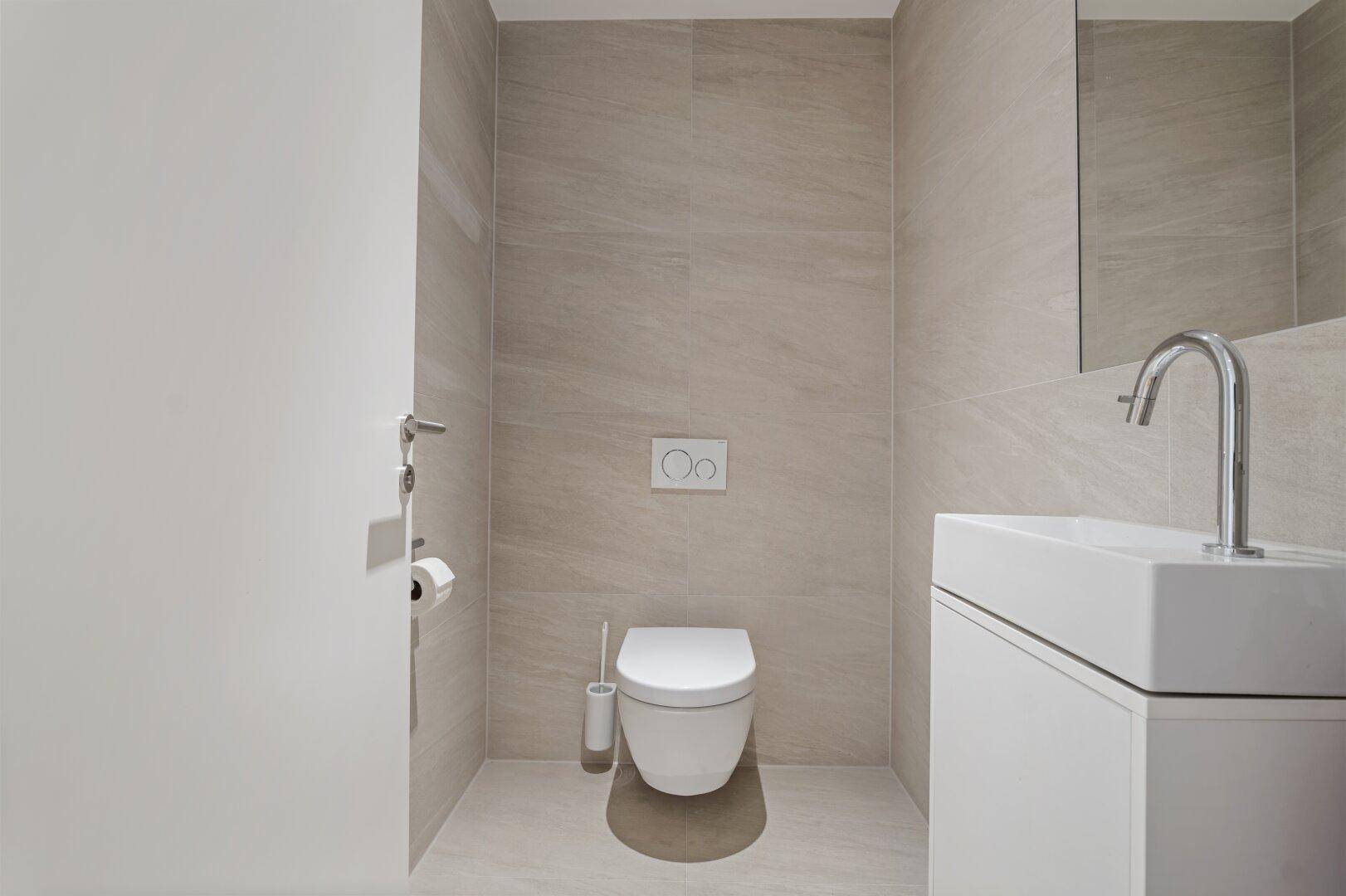 Modernes Gäste-WC mit Wand-WC, Waschbecken und hellen Fliesen.