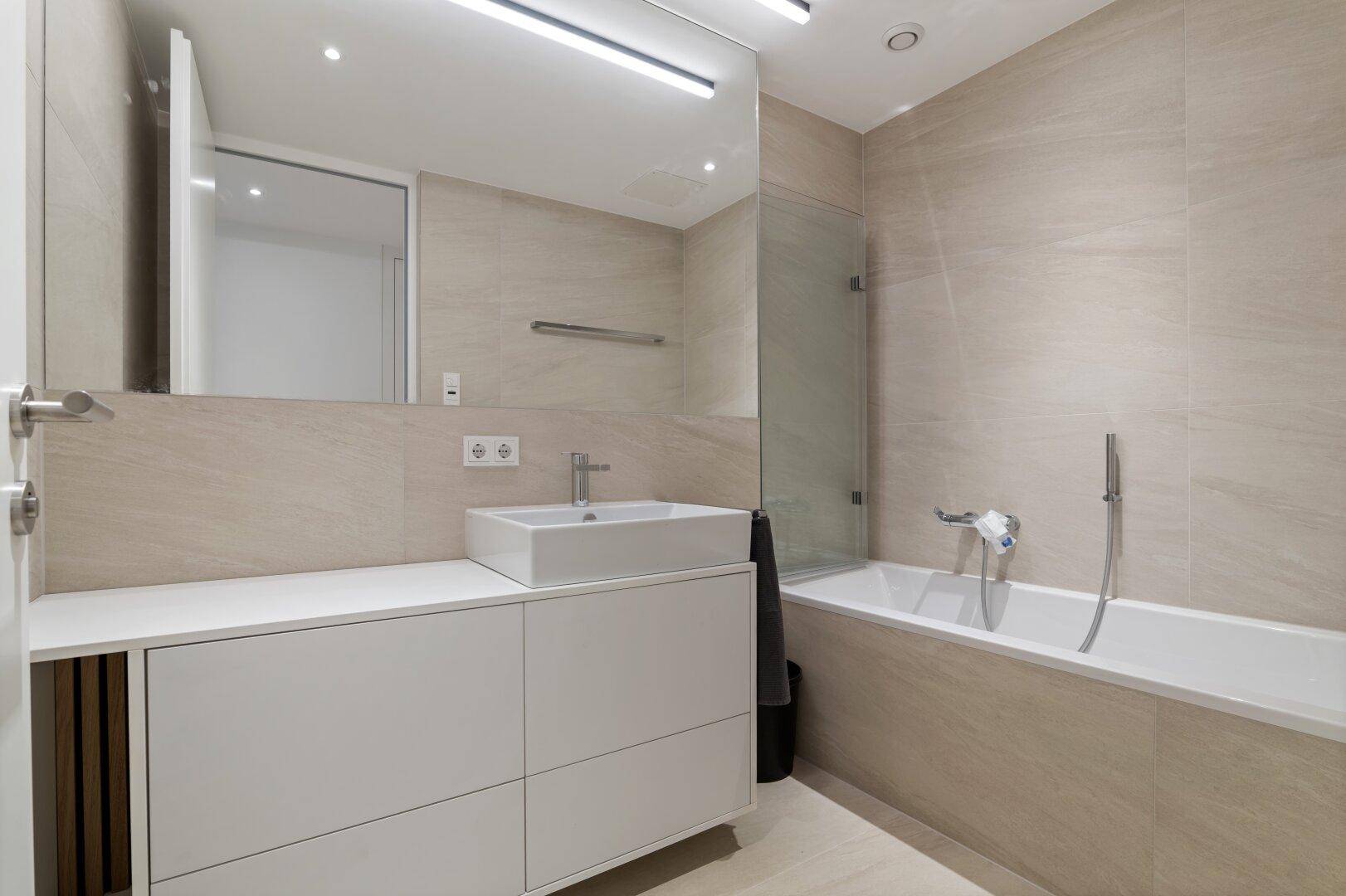 Modernes Badezimmer mit Badewanne, Waschbecken und großem Spiegel.