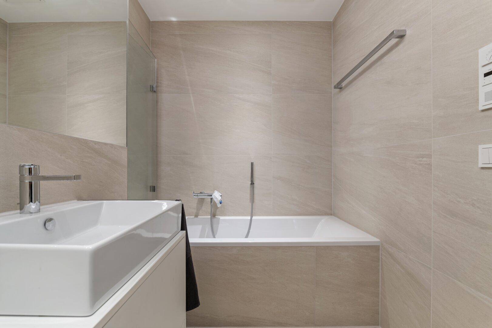 Helles Badezimmer mit Badewanne, Waschbecken und beigefarbenen Fliesen.