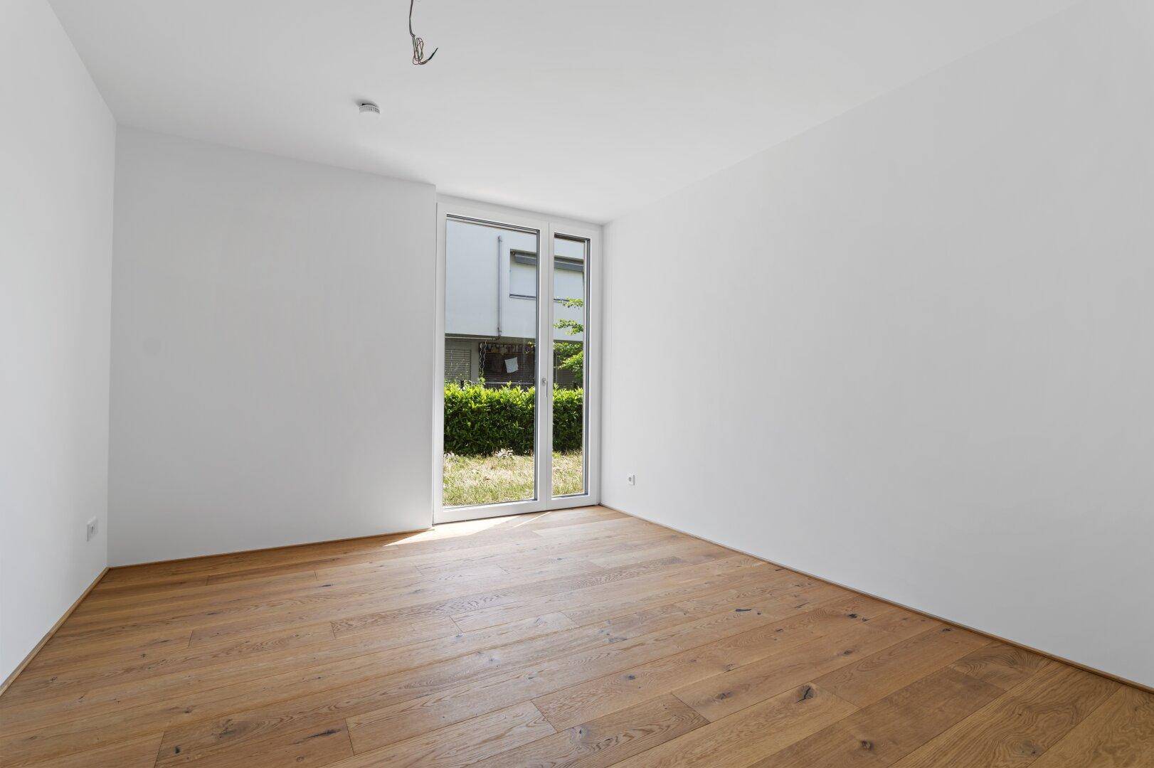 Geräumiges Schlafzimmer mit Holzboden und großen Fenstern zum Garten.