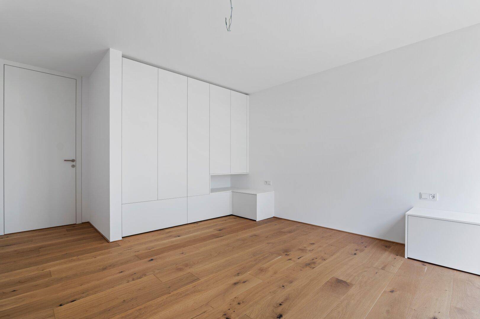 Schlafzimmer mit integrierten weißen Einbauschränken und Holzboden.