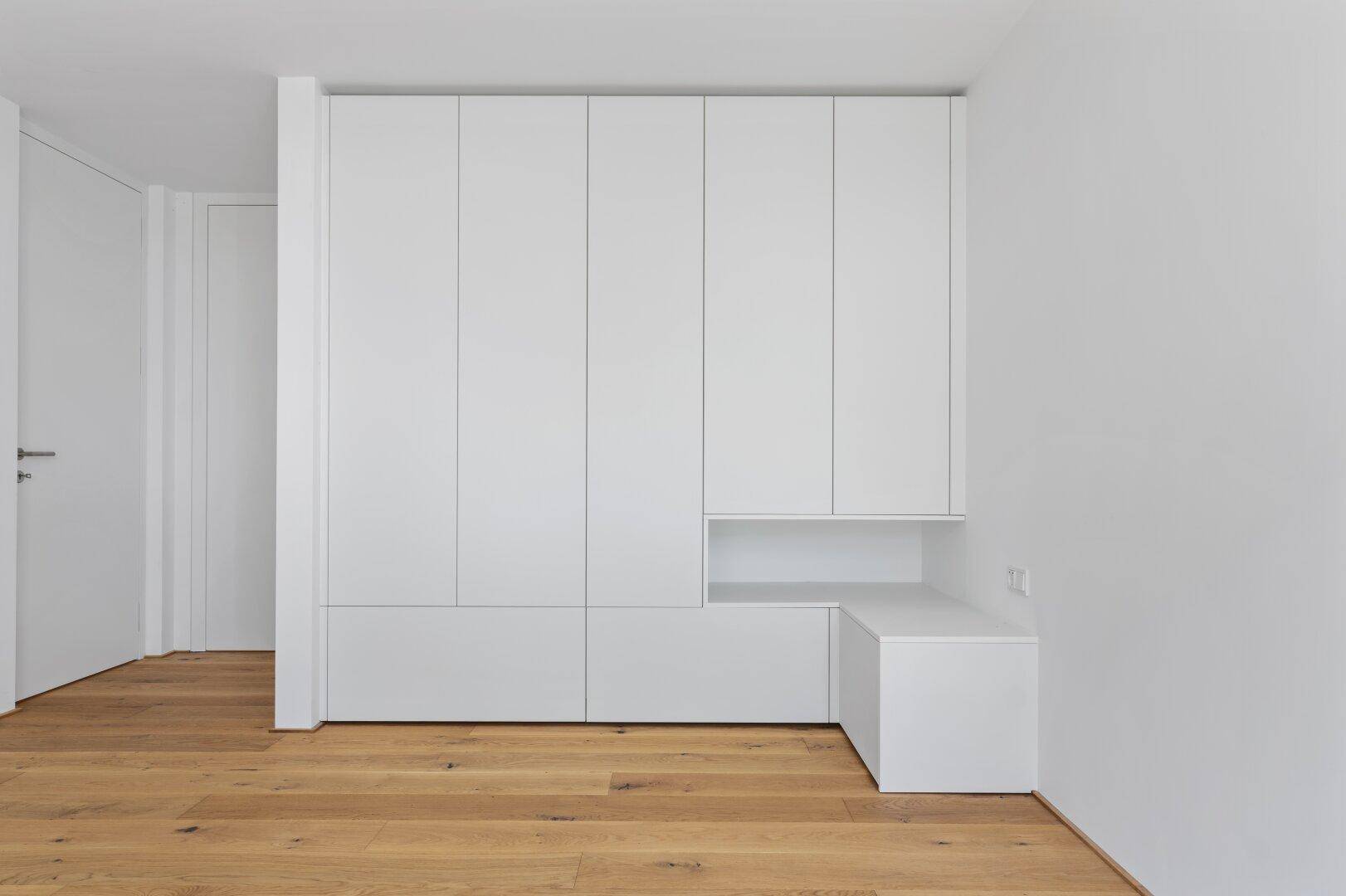 Weiße Einbauschränke im Schlafzimmer bieten viel Stauraum und eine Sitzgelegenheit.