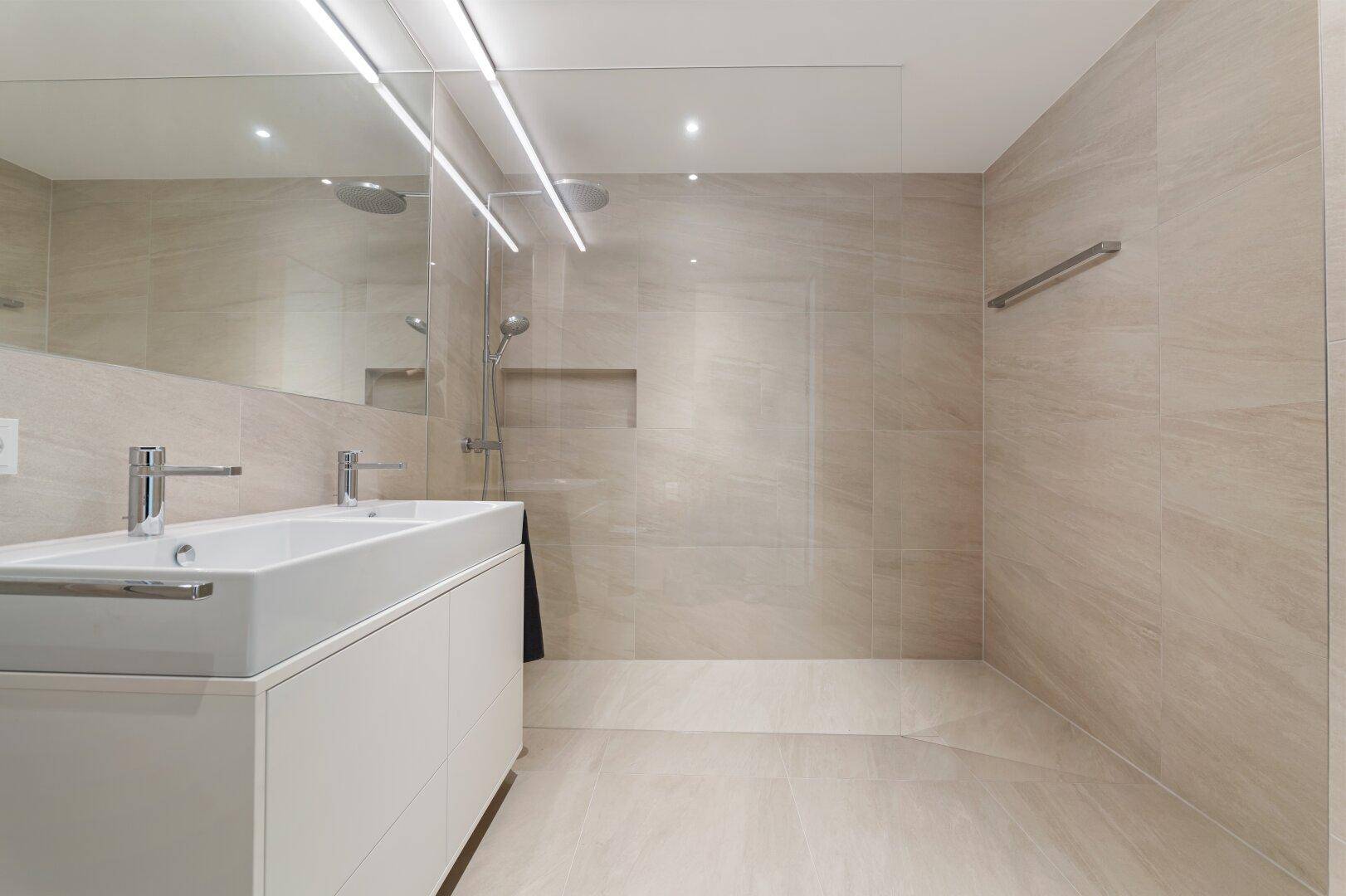 Modernes Badezimmer mit begehbarer Dusche, Doppelwaschbecken und hellen Fliesen.