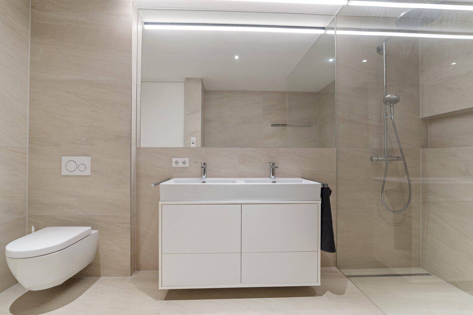 Modernes Badezimmer mit doppelten Waschbecken, begehbarer Dusche und hellen Fliesen.