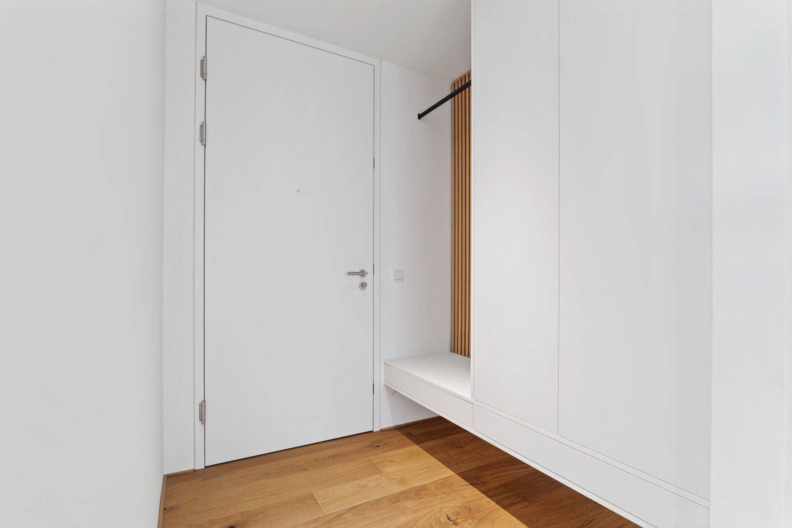 Heller Eingangsbereich mit Holzboden und integrierten weißen Einbauschränken.